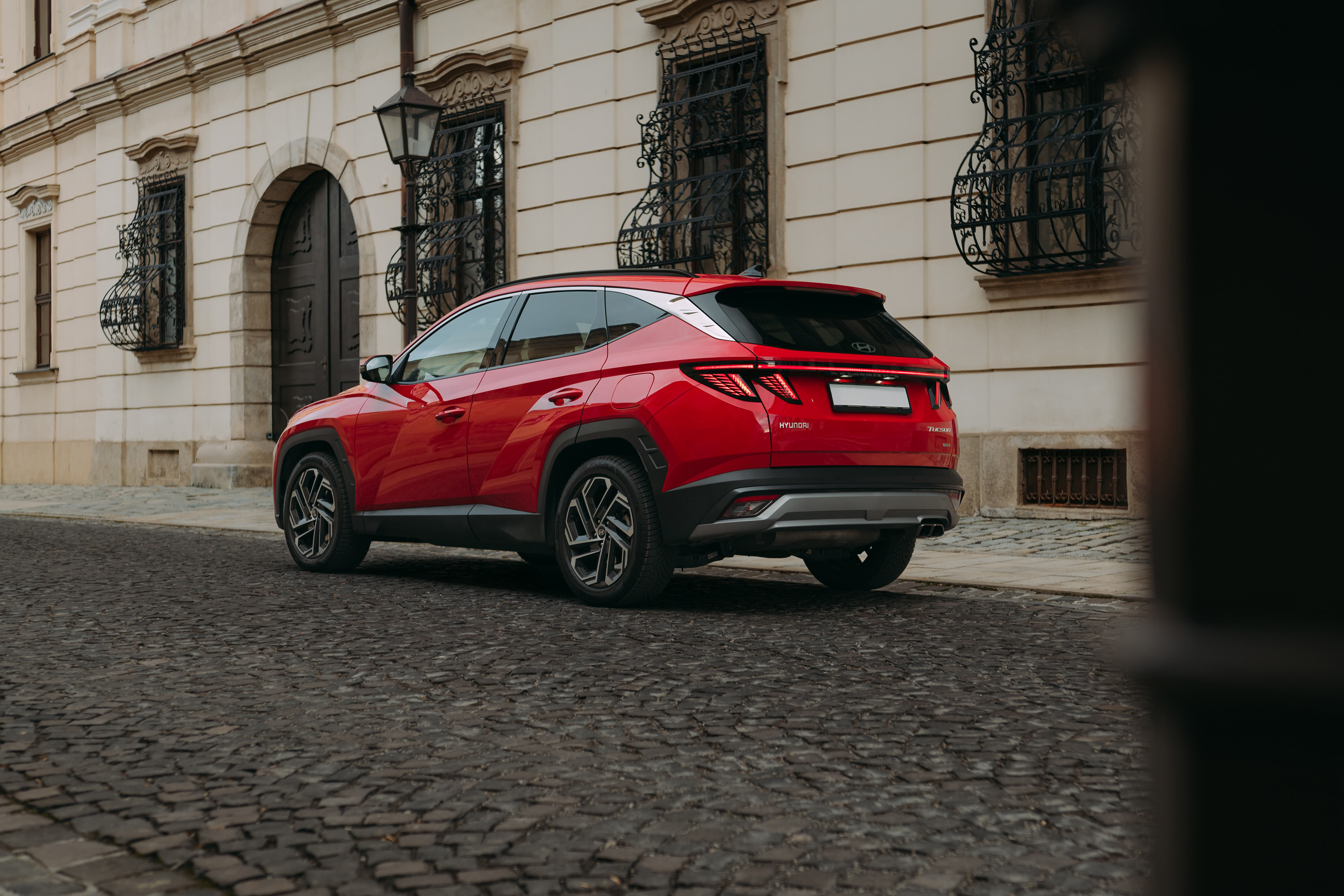 Červený Hyundai Tucson zaparkovaný na historickej ulici s dlažbou, pred budovou so zdobenými mrežami na oknách.