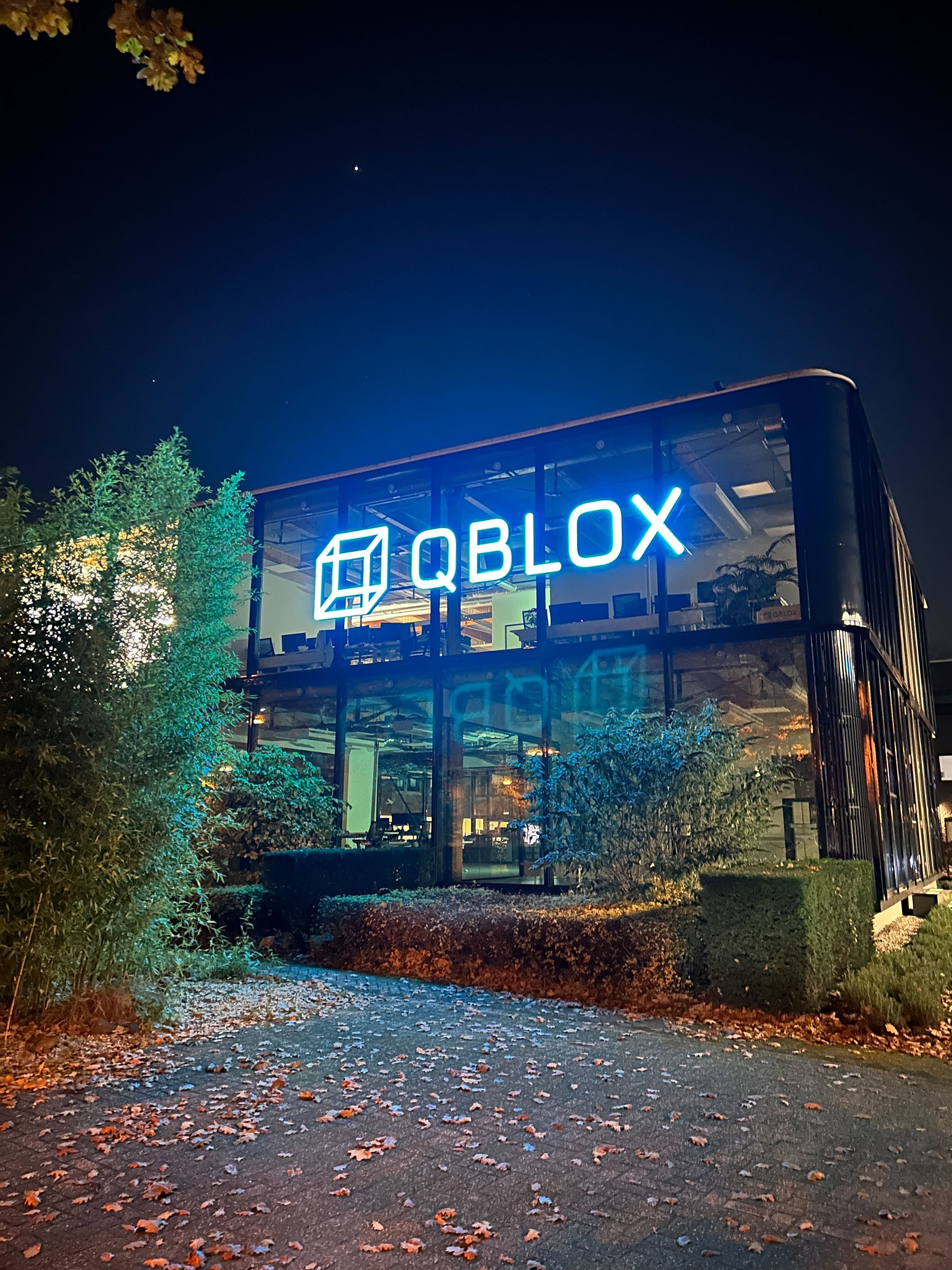Qblox Delft headquarters by night with illuminated turquoise Qblox neon sign, photo credit Pien Buurman van Vreeden.