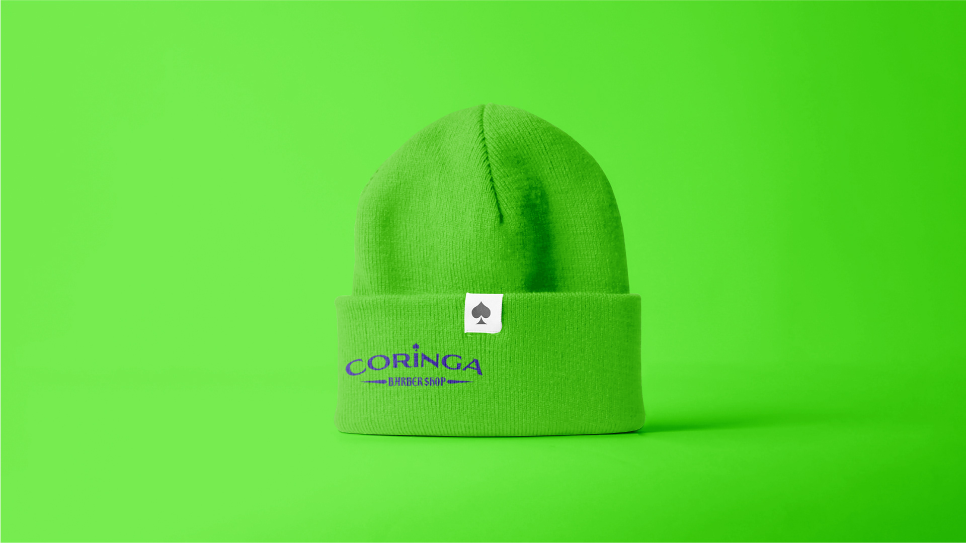 Gorro de lã verde com logo da Coringa Barber Shop bordado em roxo e uma etiqueta branca com símbolo de naipe de espadas