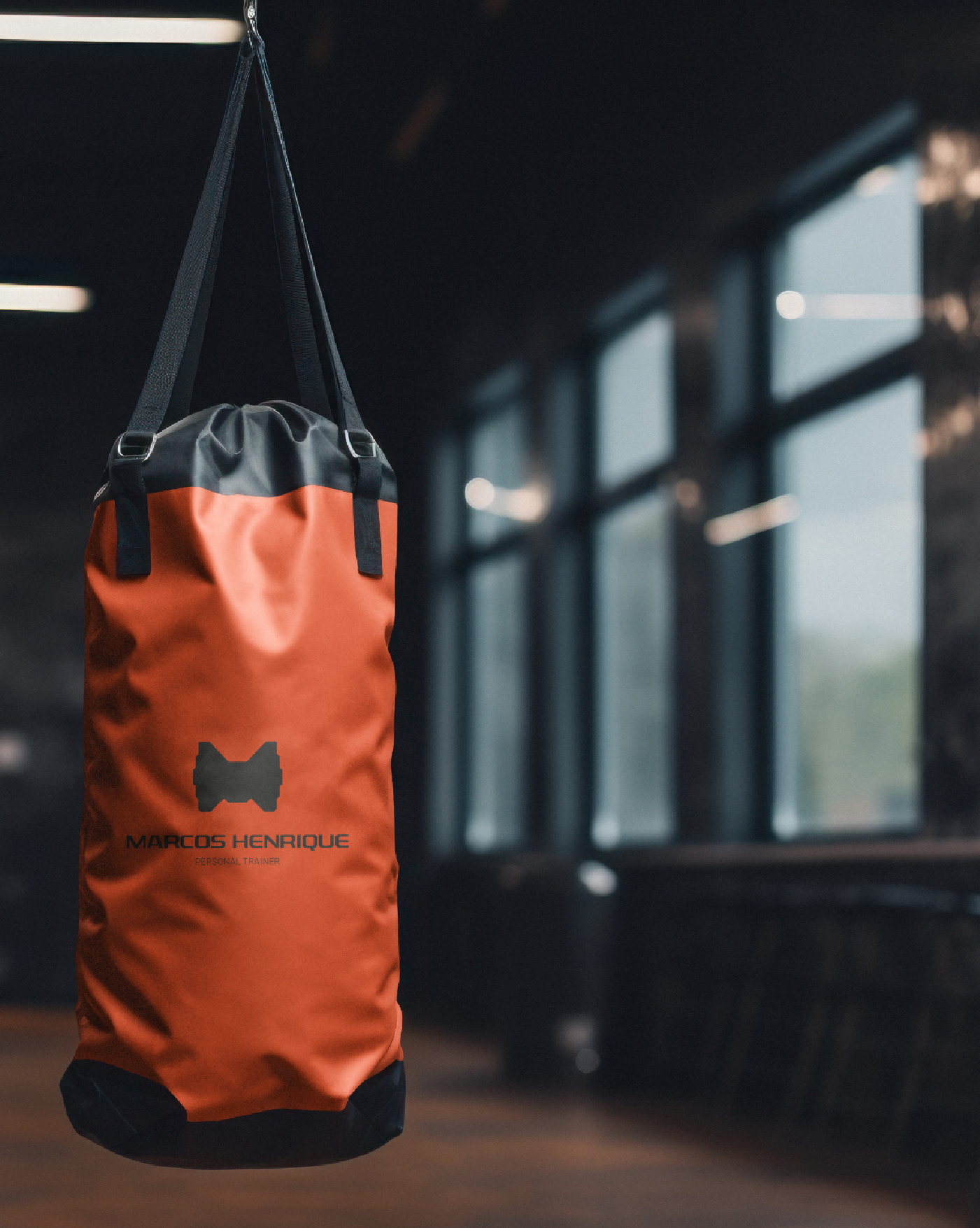 Saco de pancada laranja suspenso em academia com o logotipo de Marcos Henrique Personal Trainer aplicado, ambiente com equipamentos de treino ao fundo
