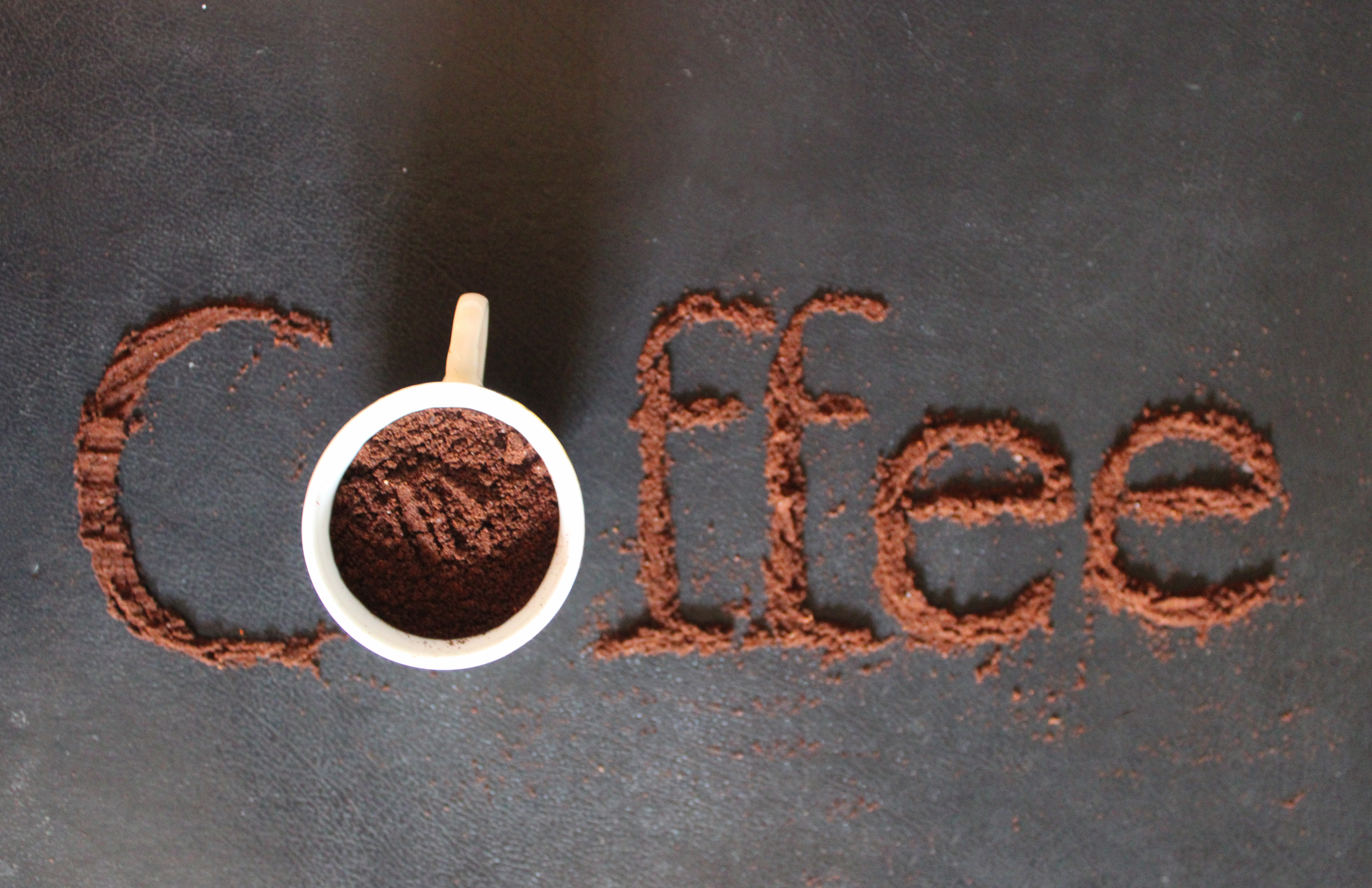 Title: Coffee Description: Coffee grounds sprinkled through text cutout against dark gray countertop Date: Fall 2024 Credits: Photography by Luisa F. Ligardo