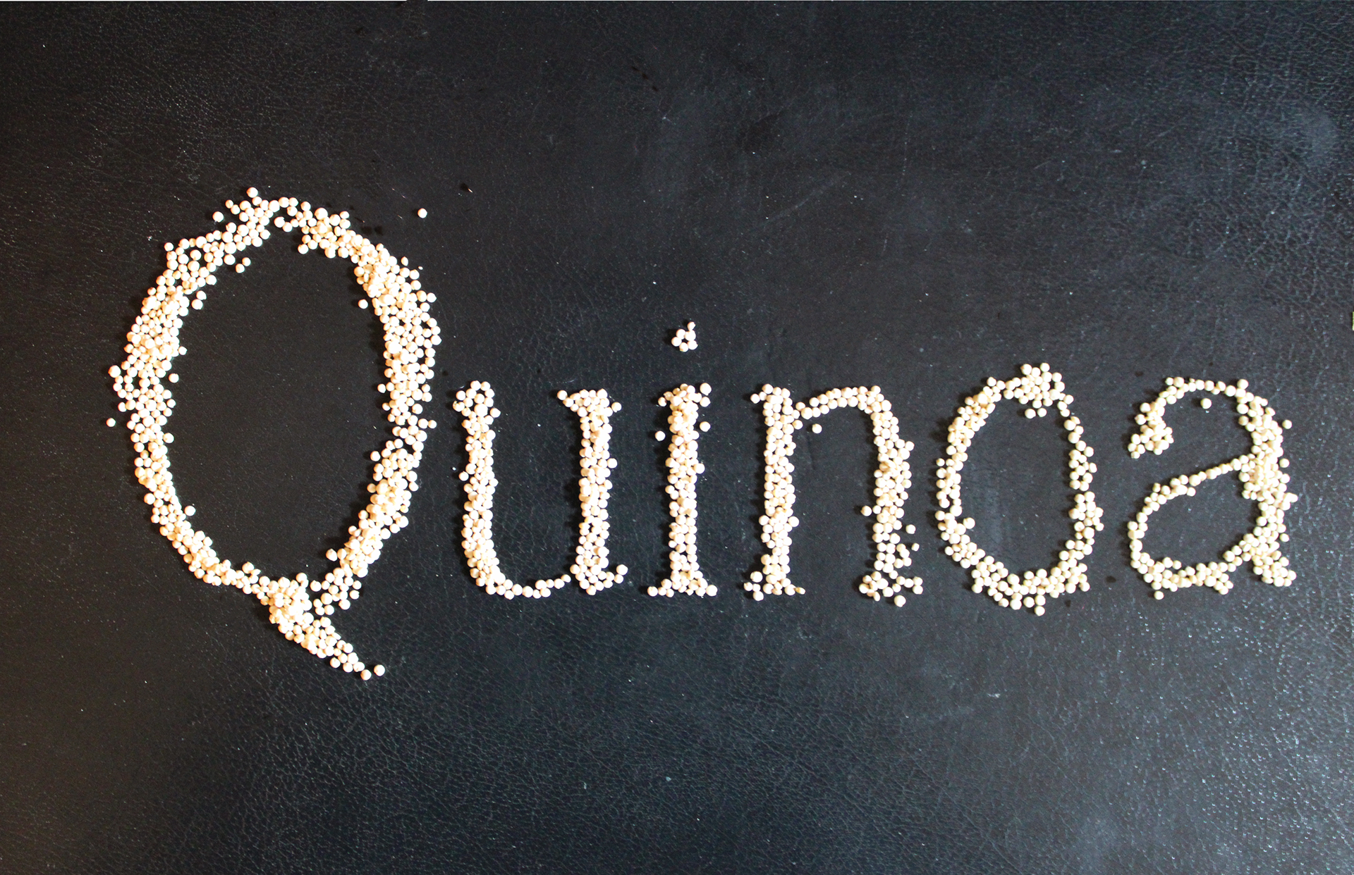 Title: Quiona Description: Quinoa seeds sprinkled through text cutout against black sketchbook Date: Fall 2024 Credits: Photography by Luisa F. Ligardo