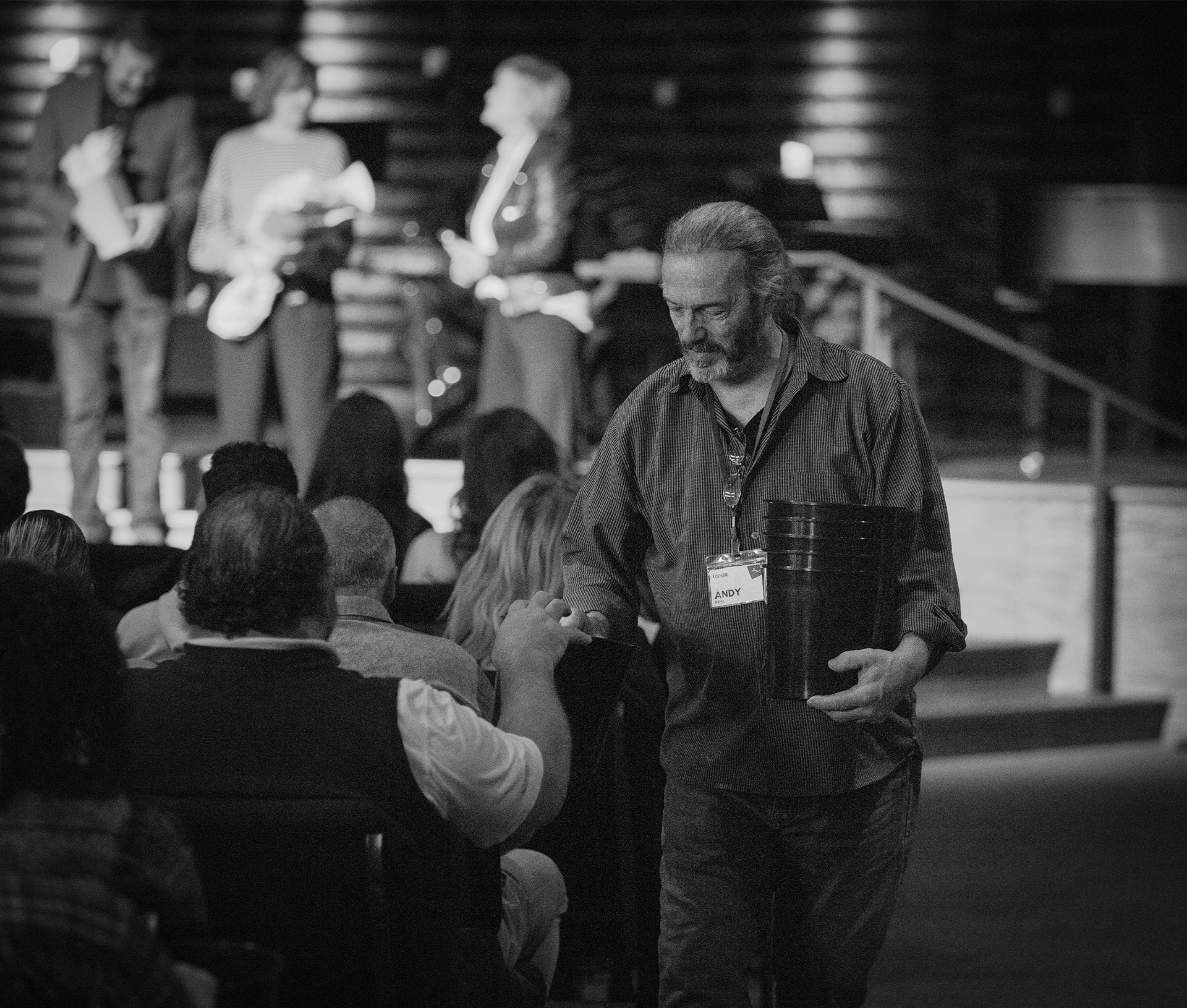 During the third service of the day, while the pastors are recognized on stage, Andy Peel transitions from ushering people to their seats to collecting offering buckets.
