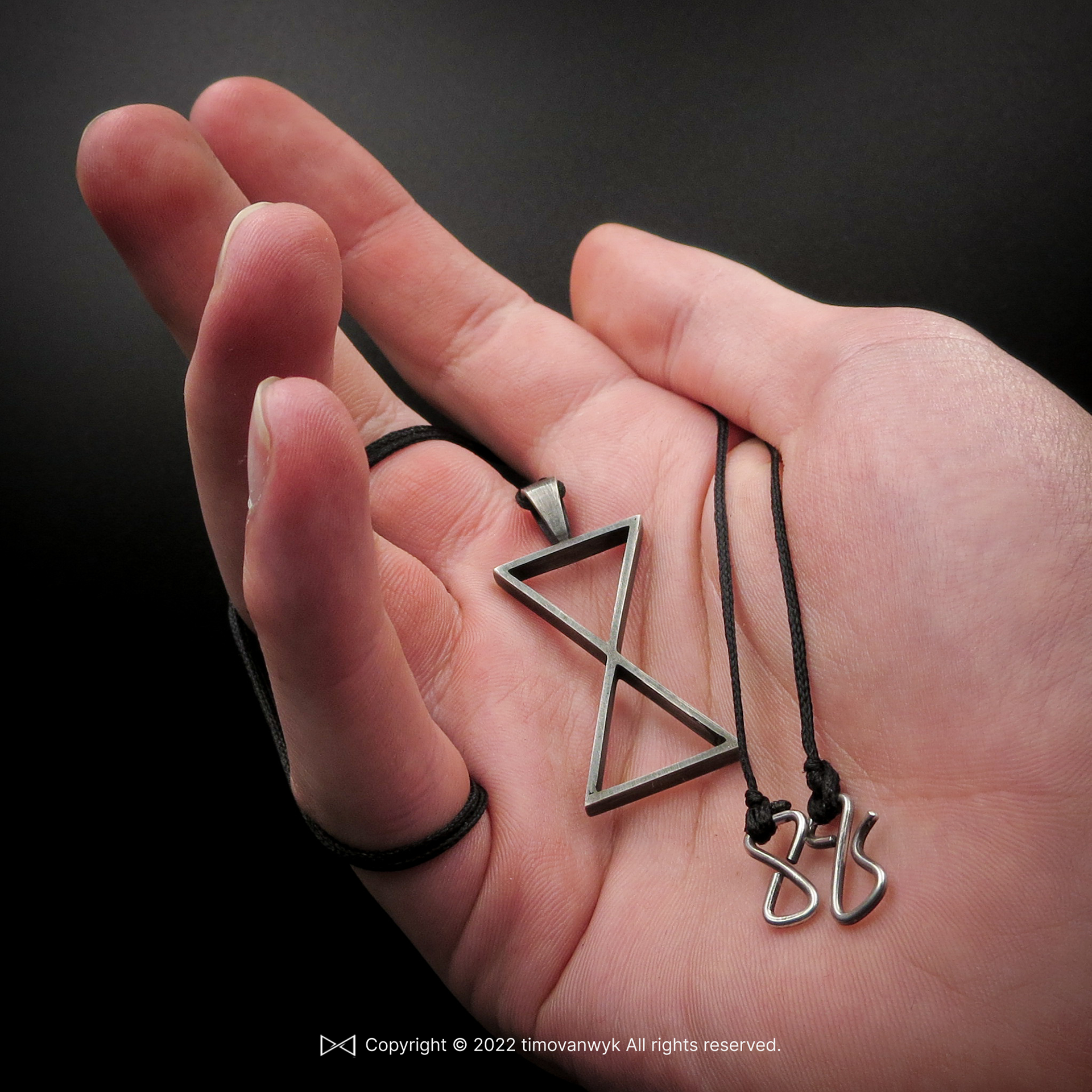 hand holding silver hour glass pendant with symbolic meaning.