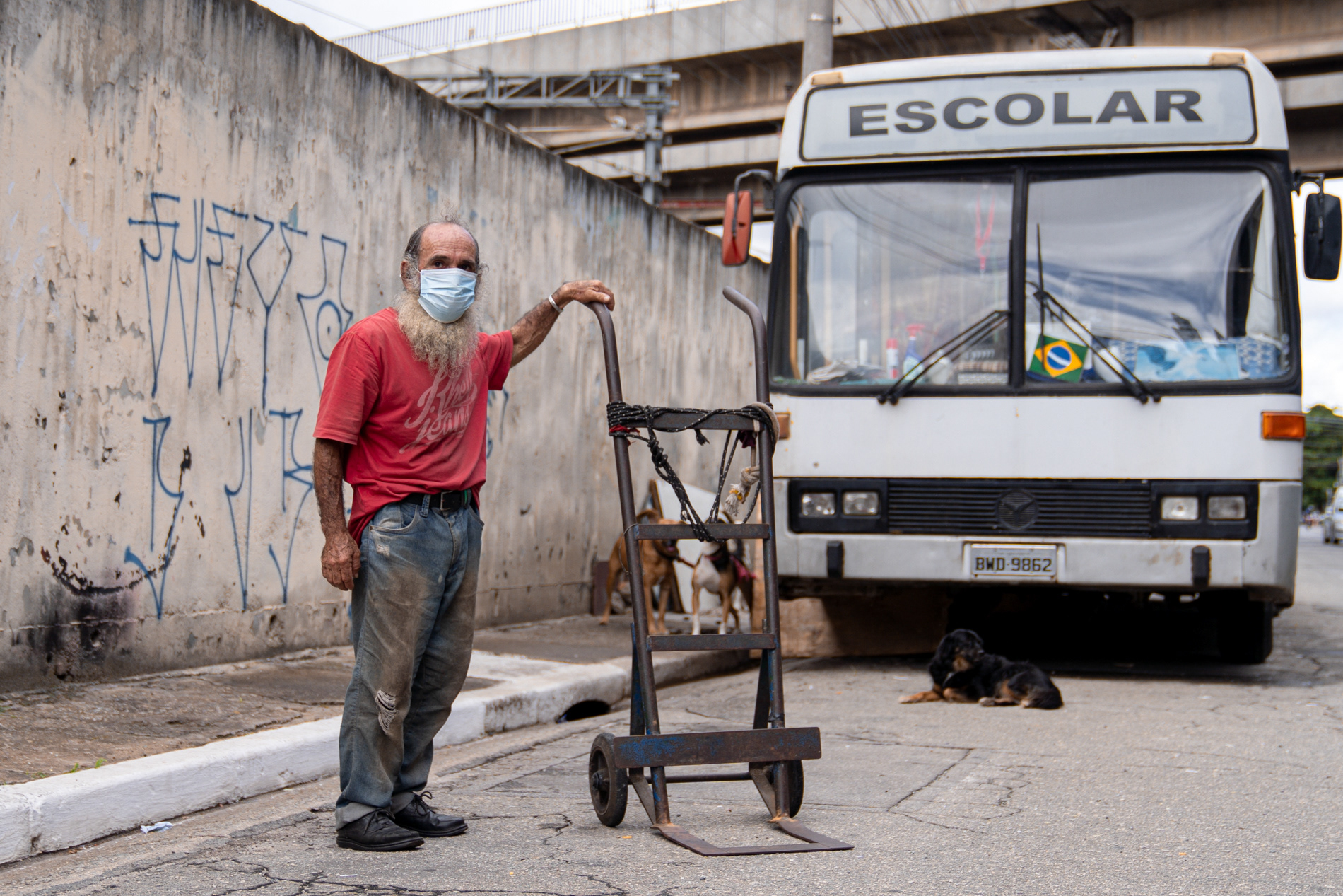 João Andrade Correia posa para foto em frente ao ônibus que divide com dez cachorros na zona leste de São Paulo, em abril de 2021