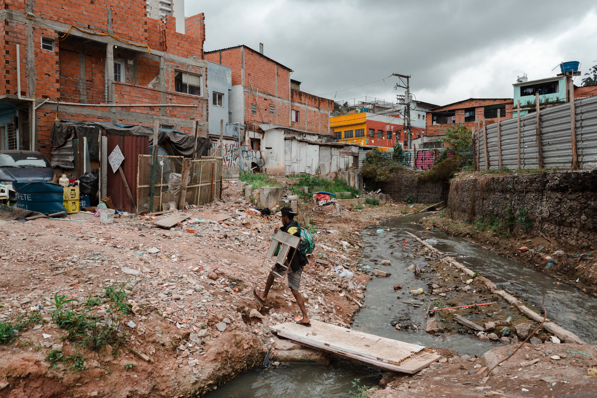 Homem caminha em ponte improvisada em córrego no Jardim Colombo, em São Paulo, em setembro de 2018