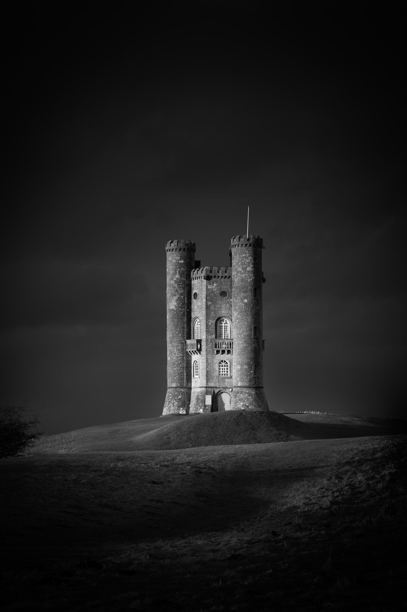 Broadway Tower hit by brief sunlight with storm clouds behind.