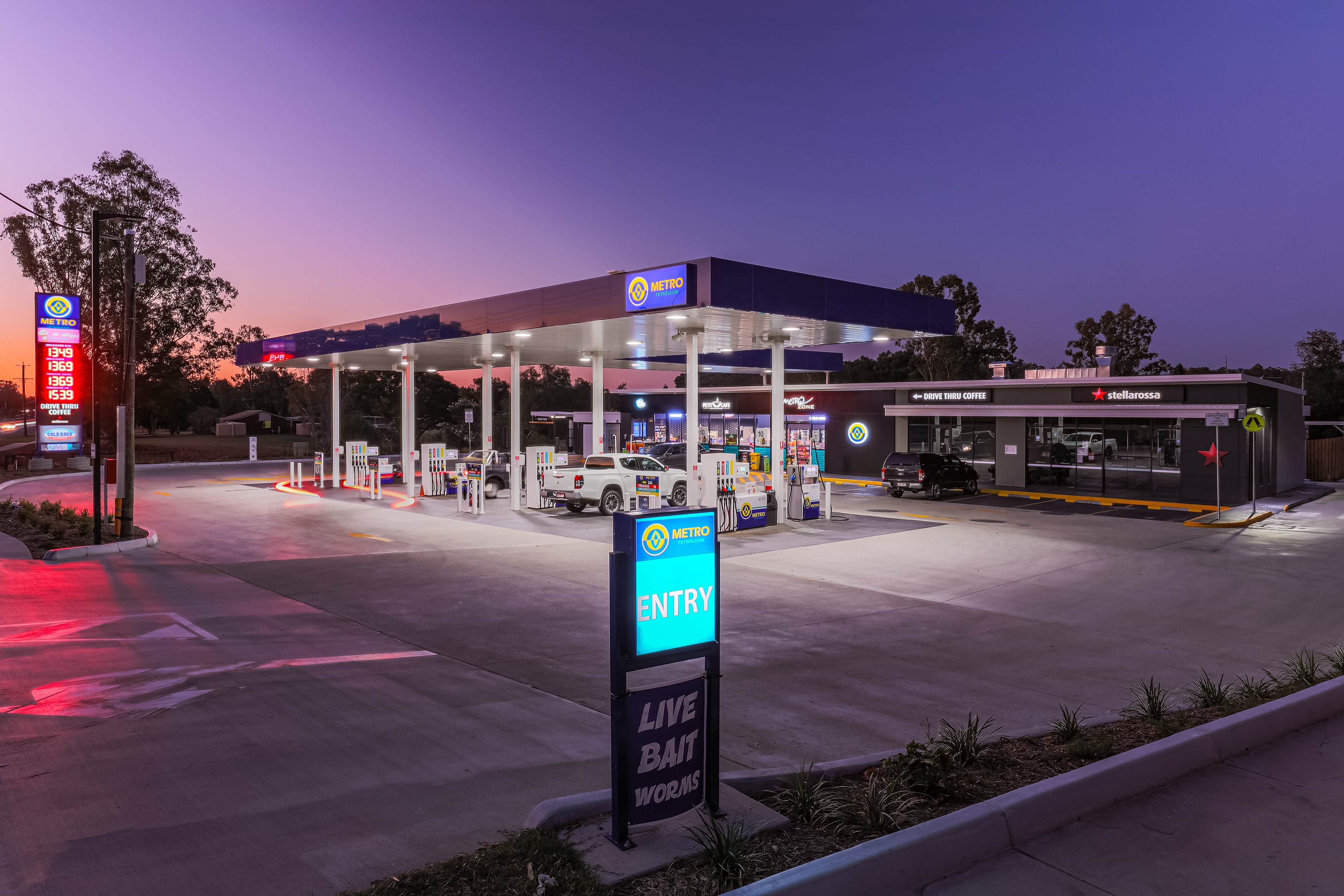 Illuminated gas station at dusk with vibrant lighting and a drive-thru coffee shop, capturing a busy yet serene evening atmosphere, located in Ipswich, QLD. Professional commercial photography by Jeremy Murphy.