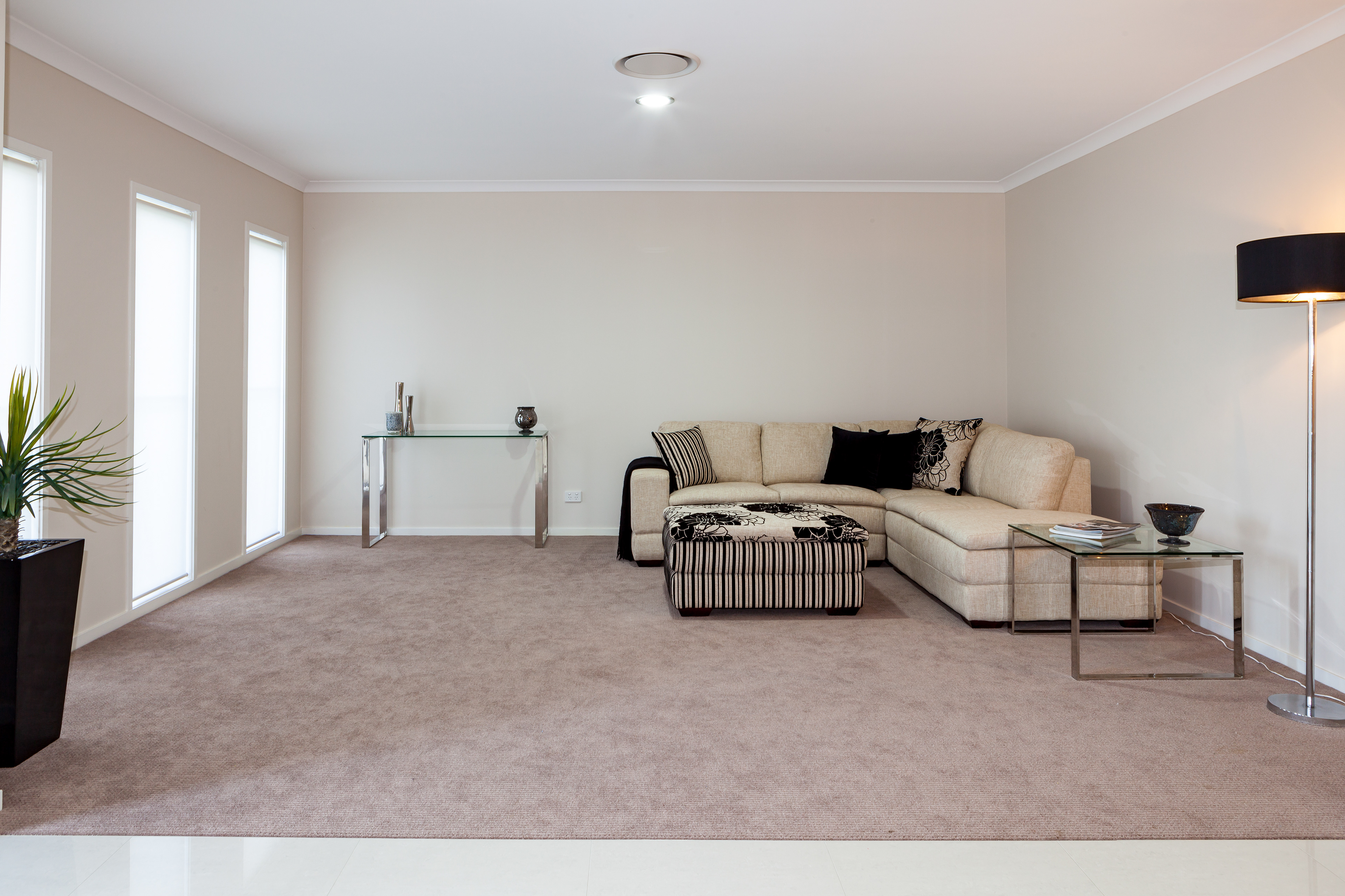 Modern living room with neutral tones featuring a beige sectional sofa, glass coffee table, floor lamp, and minimalist decor, located in Brisbane, QLD. Professional real estate photography by Jeremy Murphy.