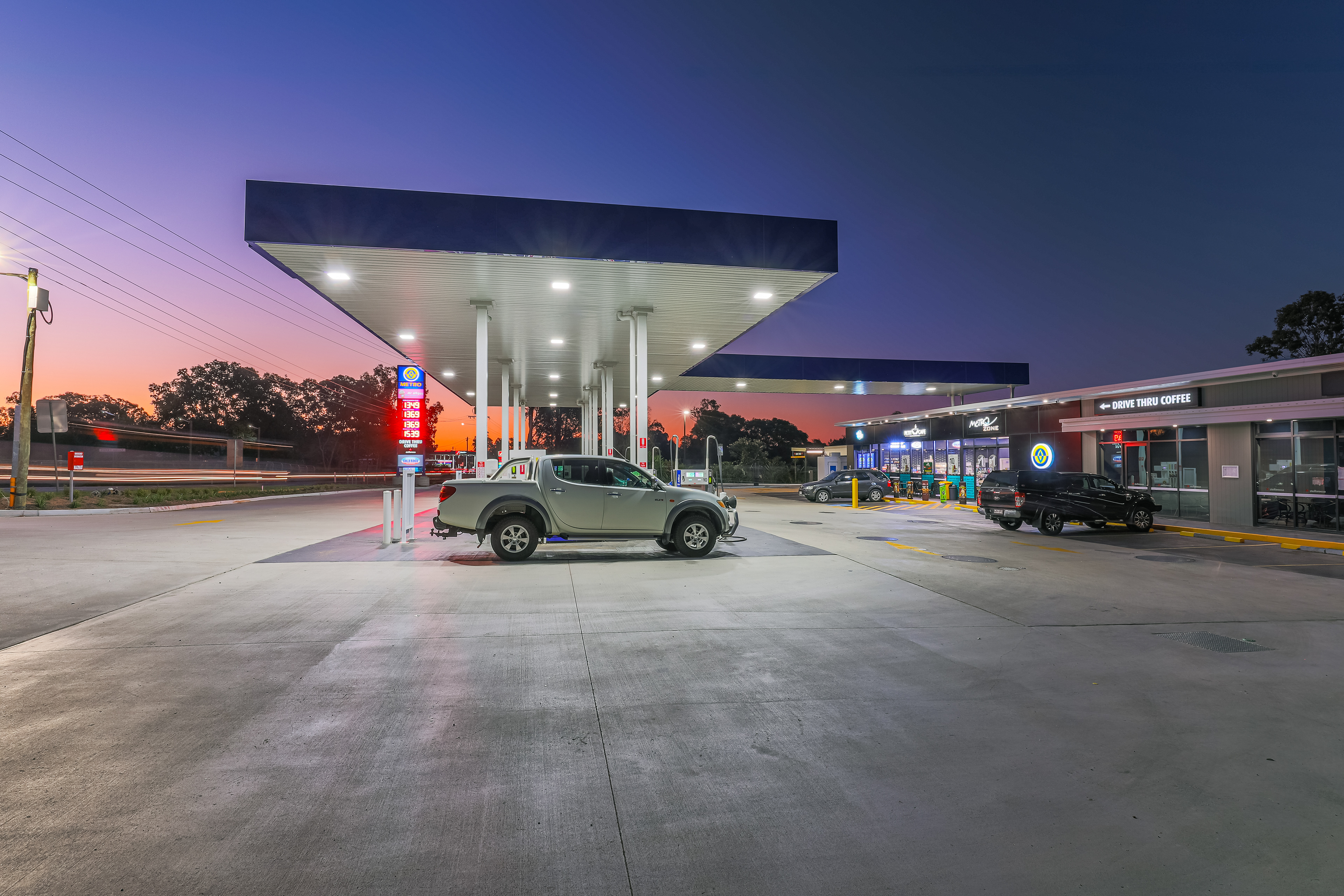 Modern gas station with drive-thru coffee shop, illuminated at dusk to highlight its amenities and accessibility, located in Brisbane, QLD. Professional commercial photography by Jeremy Murphy.
