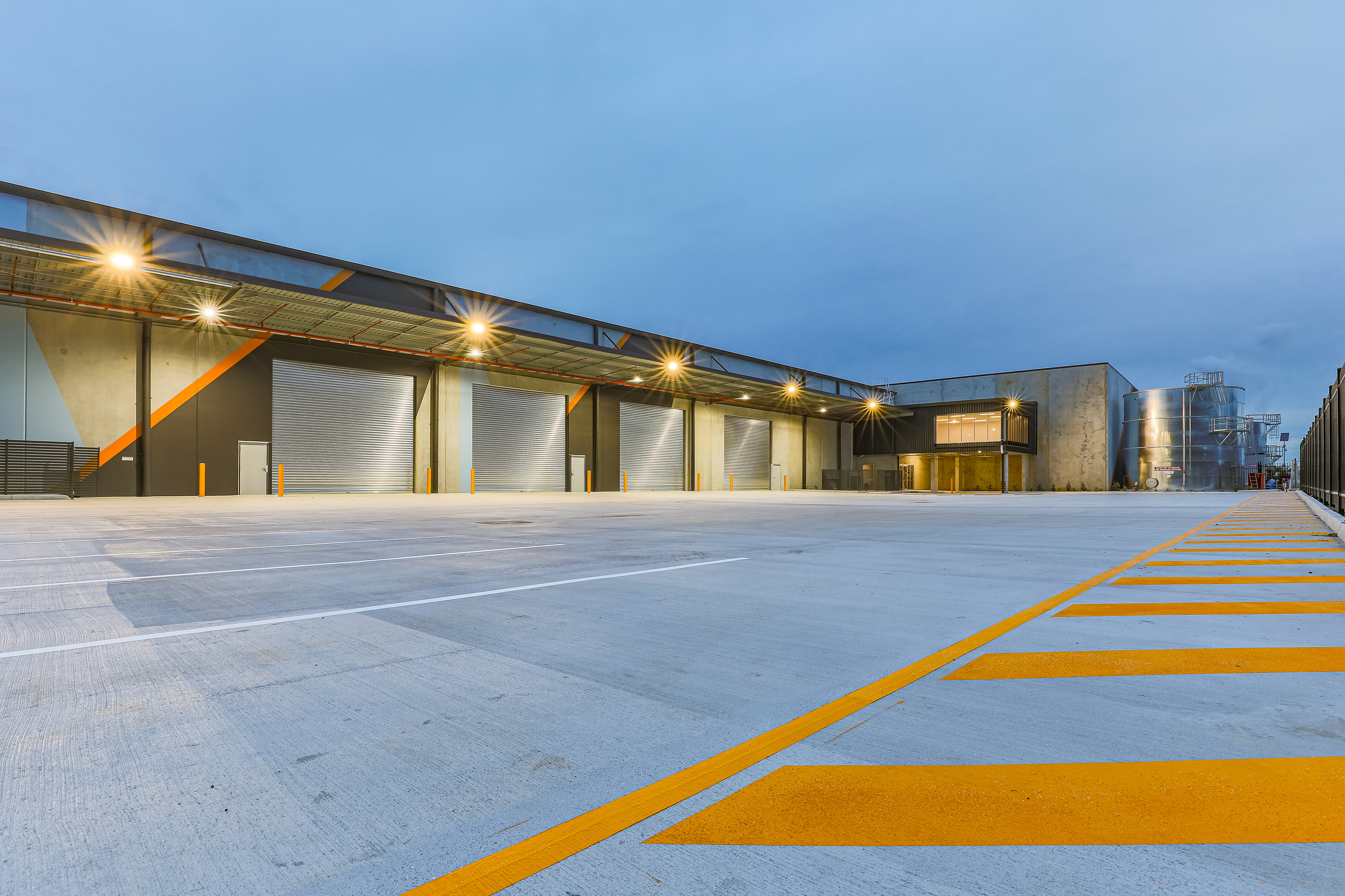 Large industrial facility with multiple loading docks and expansive outdoor space, captured in the evening with detailed lighting, located in Ipswich, QLD. Professional commercial photography by Jeremy Murphy.