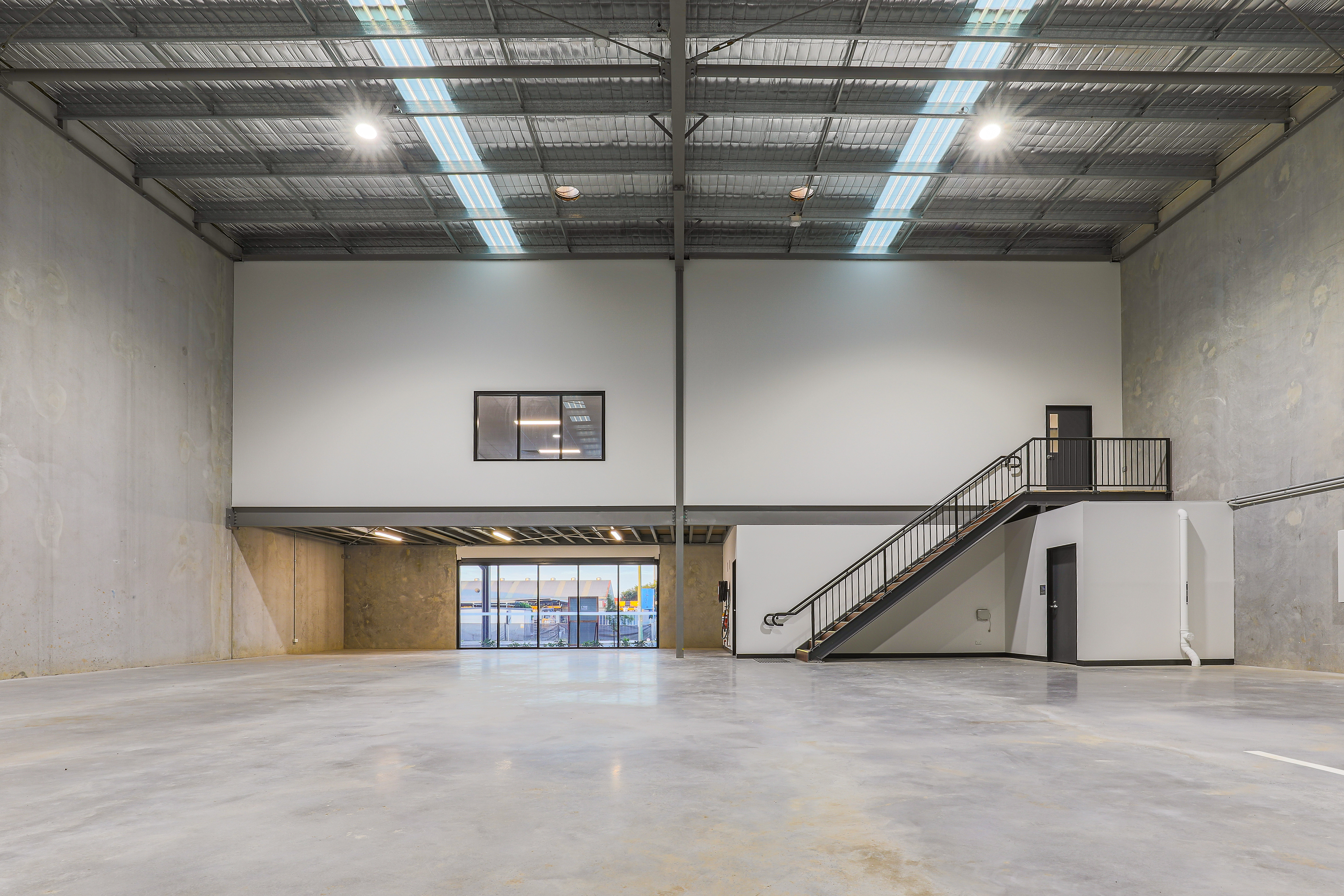 Spacious interior of a modern warehouse with high ceilings, natural light, and a mezzanine level, designed for versatility and efficiency, located in Brisbane, QLD. Professional commercial photography by Jeremy Murphy