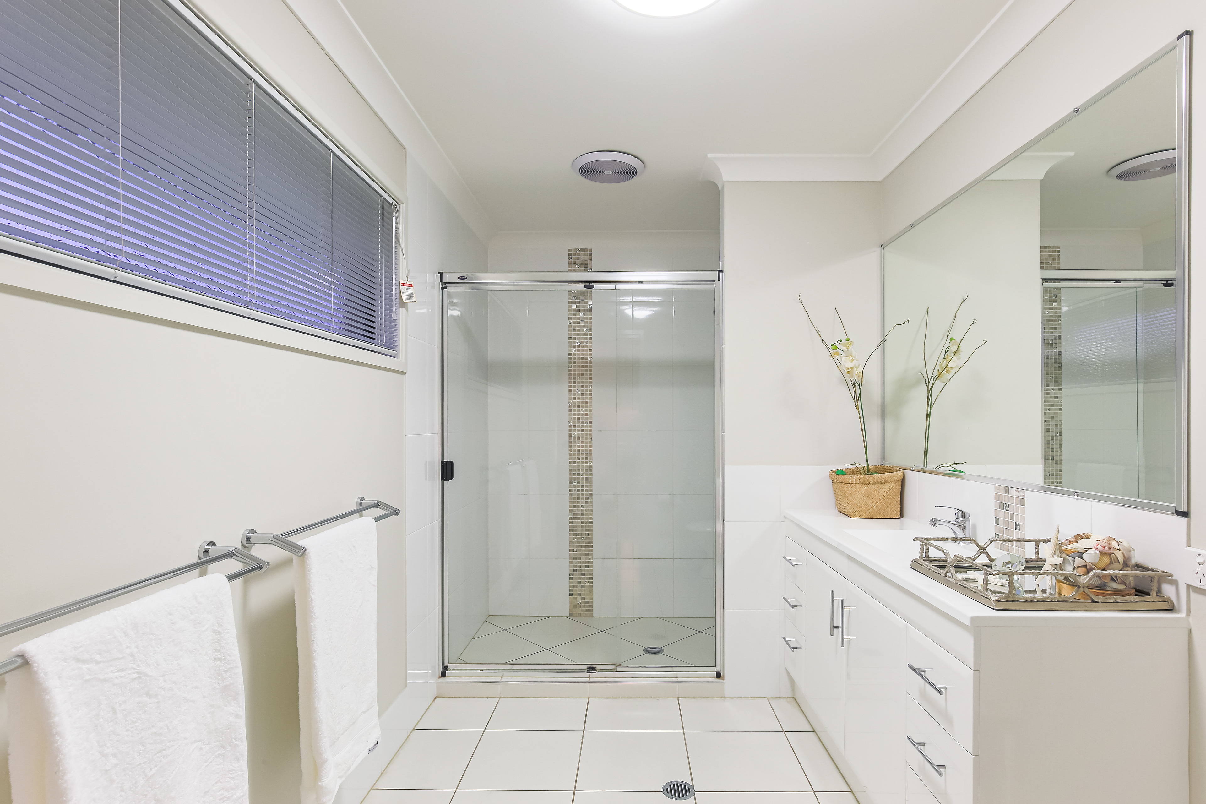 Elegant bathroom with a large glass-enclosed shower, spacious vanity with dual sinks, and minimalist decor, featuring natural light from a horizontal window, located in Ipswich, QLD. Professional real estate photography by Jeremy Murphy.