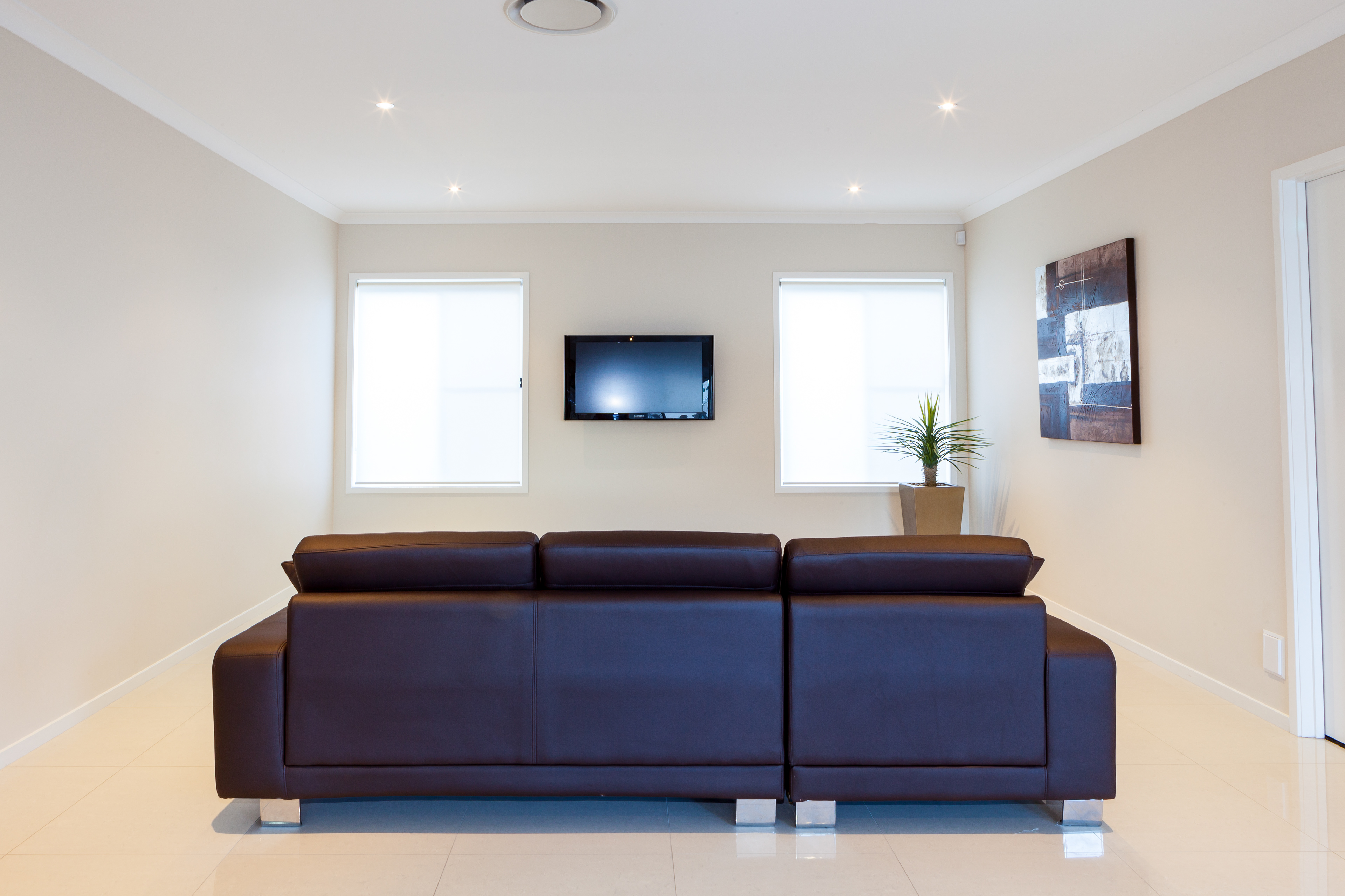 Contemporary living room with a sleek brown leather sofa, wall-mounted TV, and minimalist decor, featuring large windows for natural light, located in Brisbane, QLD. Professional real estate photography by Jeremy Murphy.