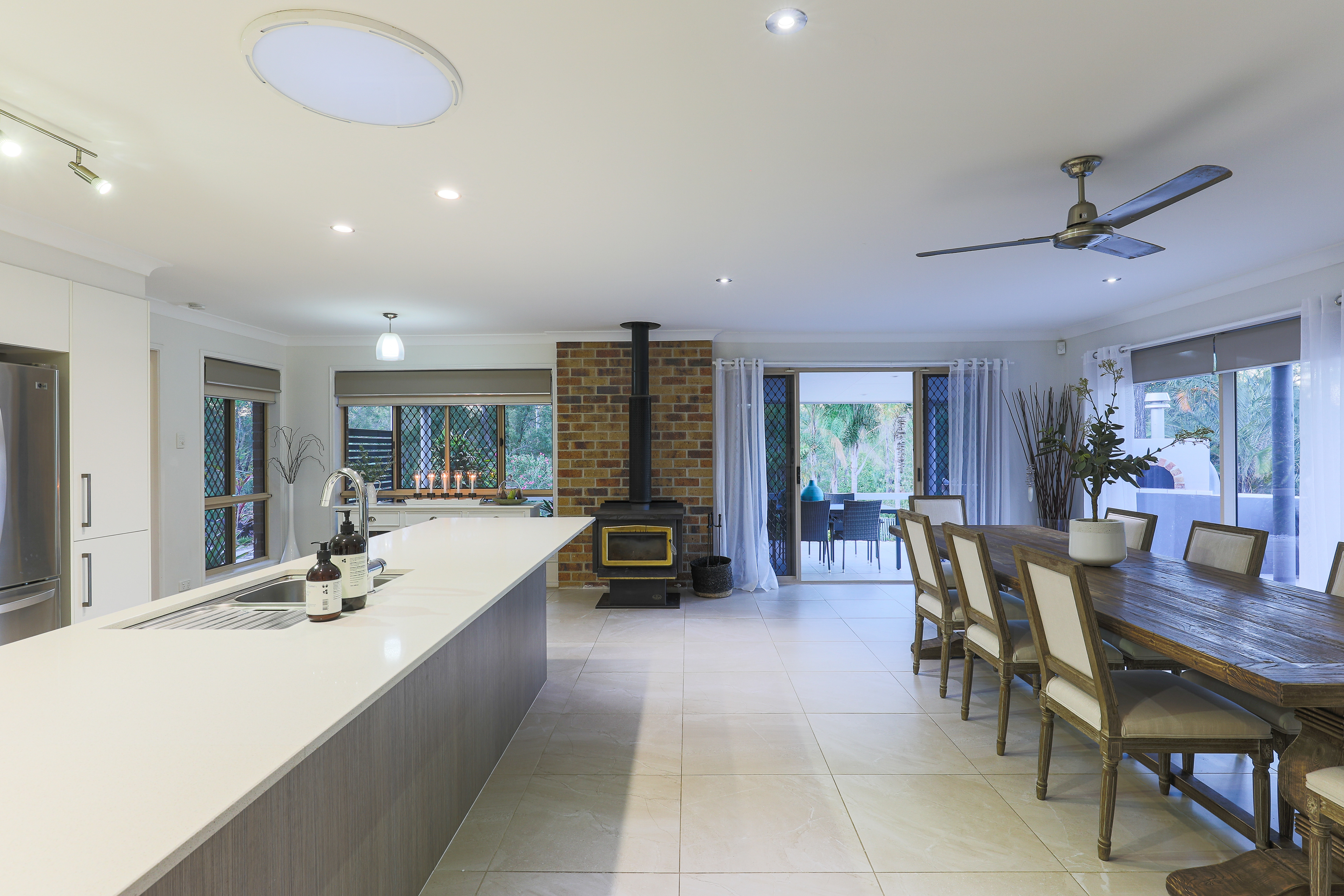 Spacious open-plan kitchen and dining area with modern appliances, a large island, wooden dining table, and cozy fireplace, located in Ipswich, QLD. Professional real estate photography by Jeremy Murphy.