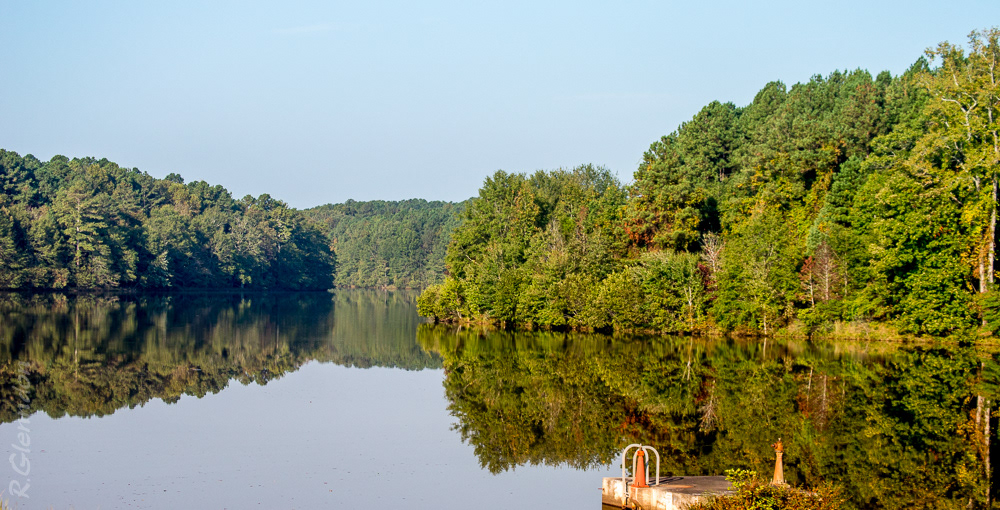 calm lake surrounded by trees reflecting sky and shoreline