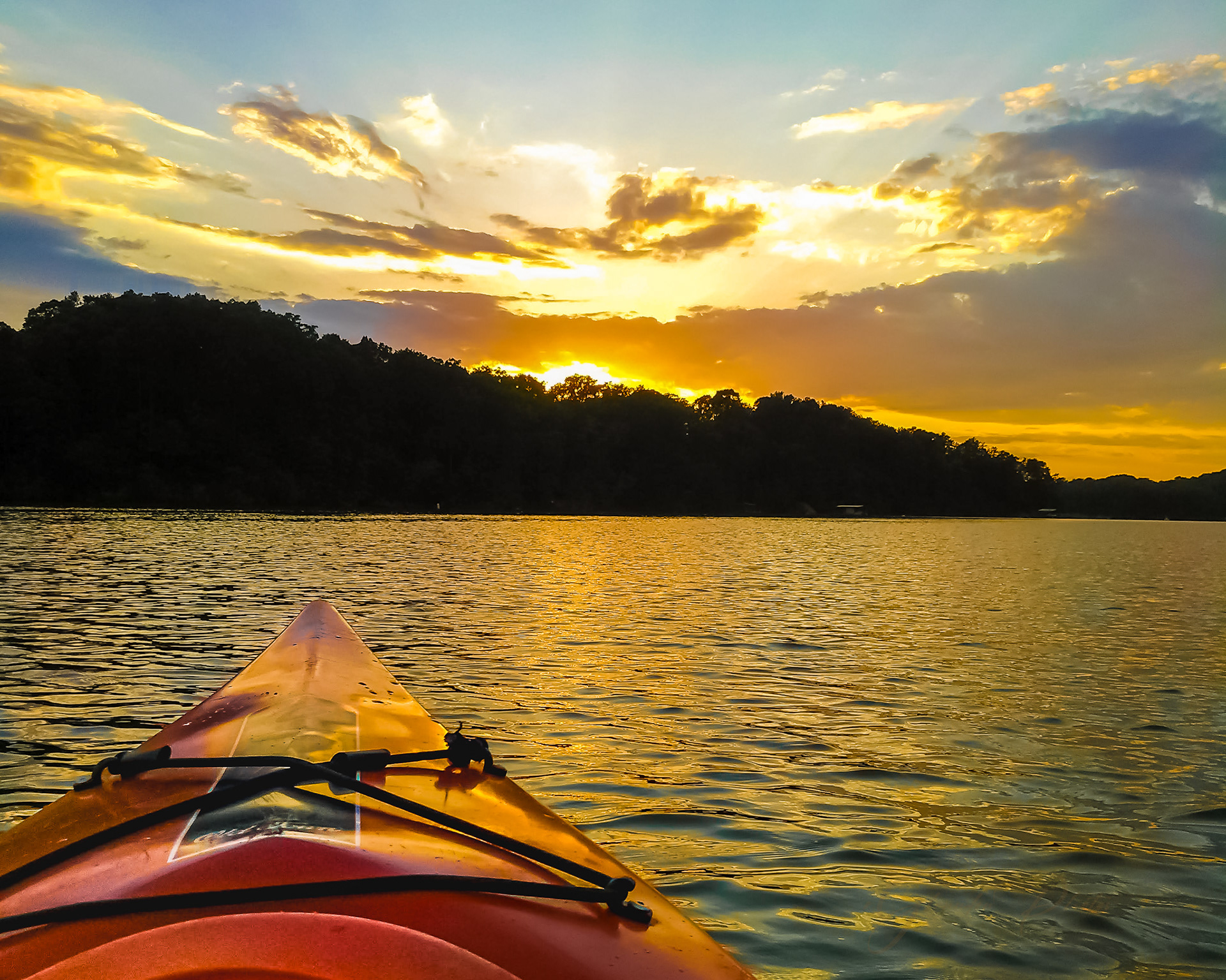 kayak on lake at sunset with golden clouds reflected on water