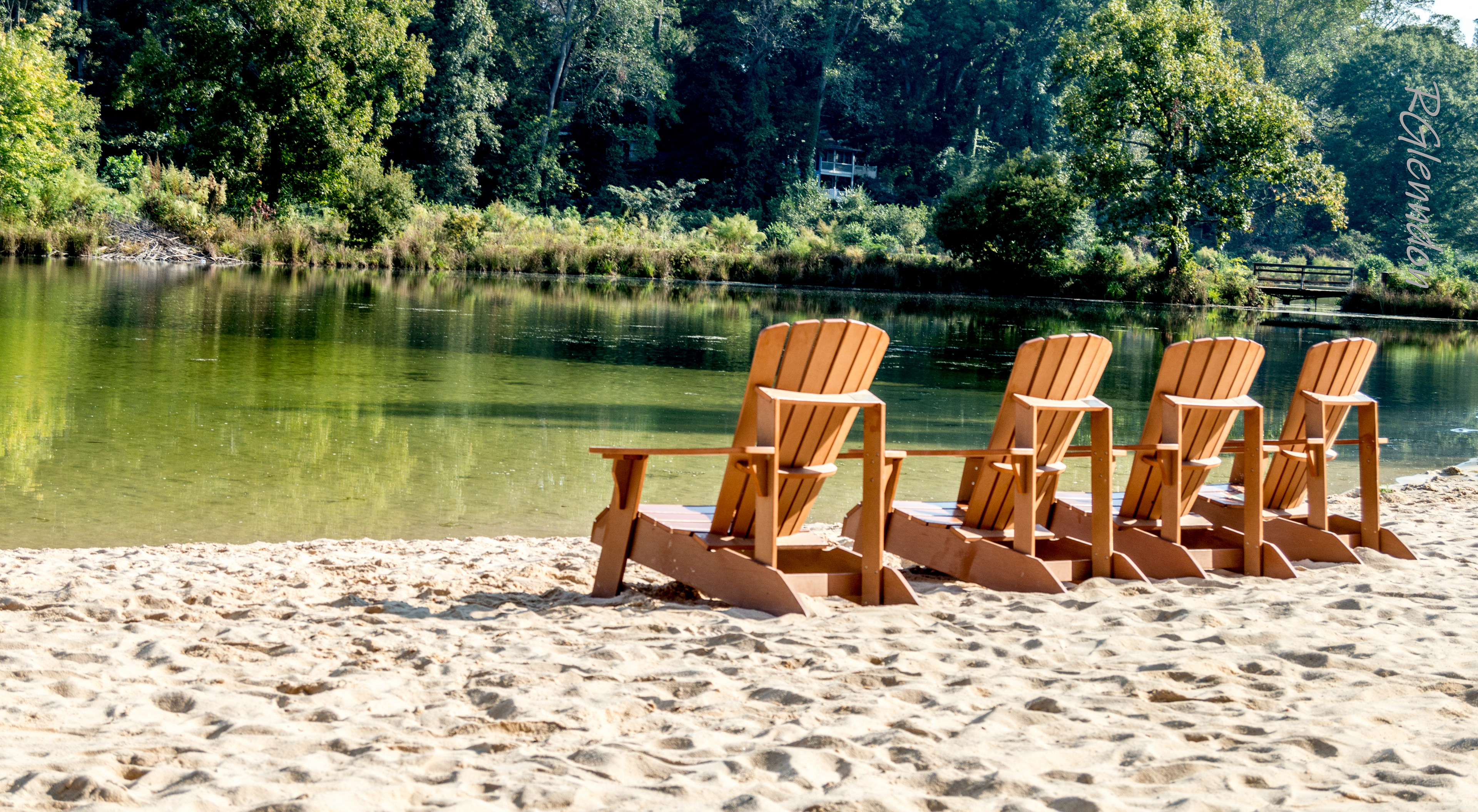 wooden chairs arranged on sandy beach beside calm lake