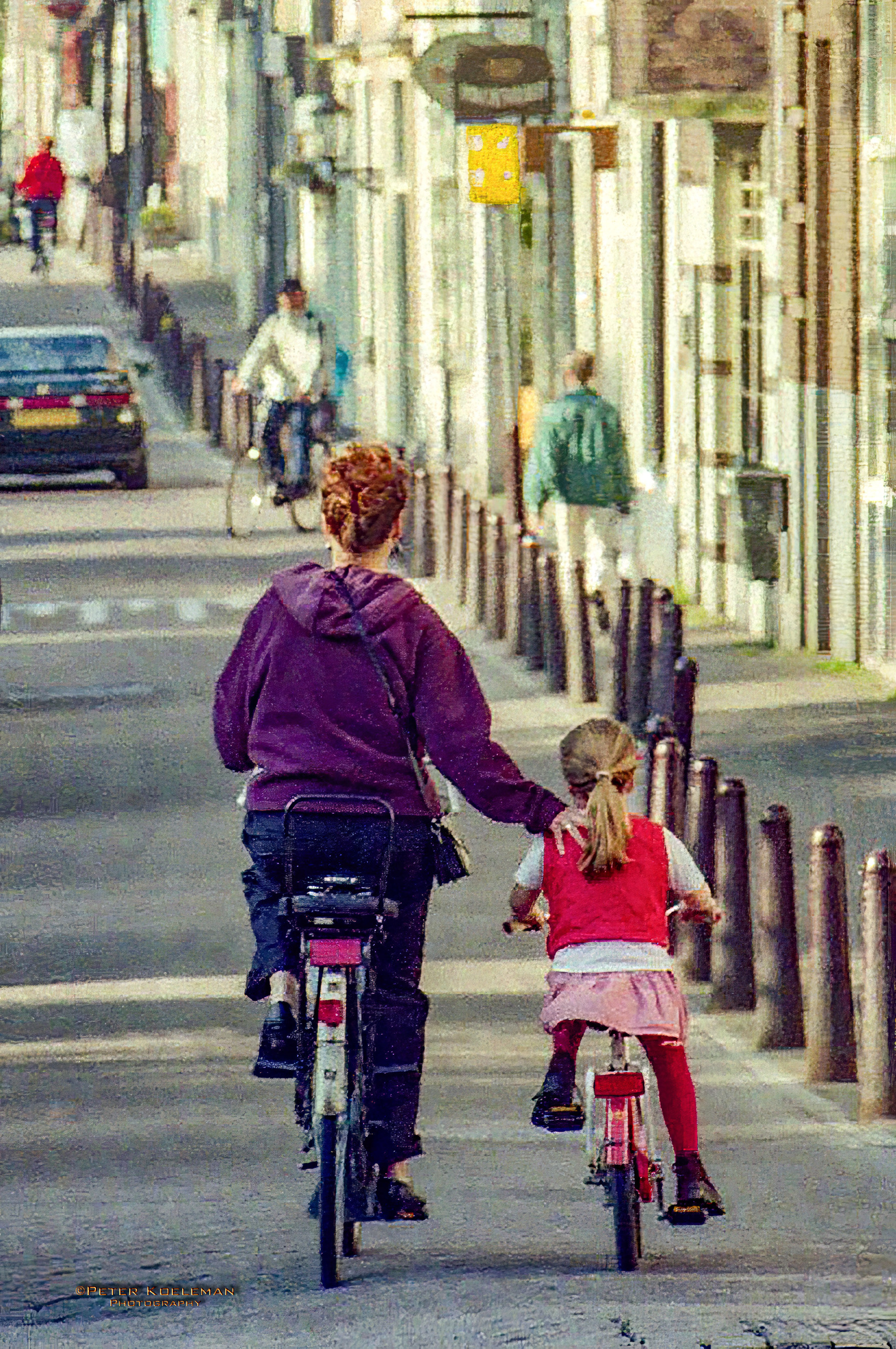 Mother & Daughter Biking on an Amsterdam Street - It is a very common site to see this: a mother with a protective hand on her young daughter while riding bicycles