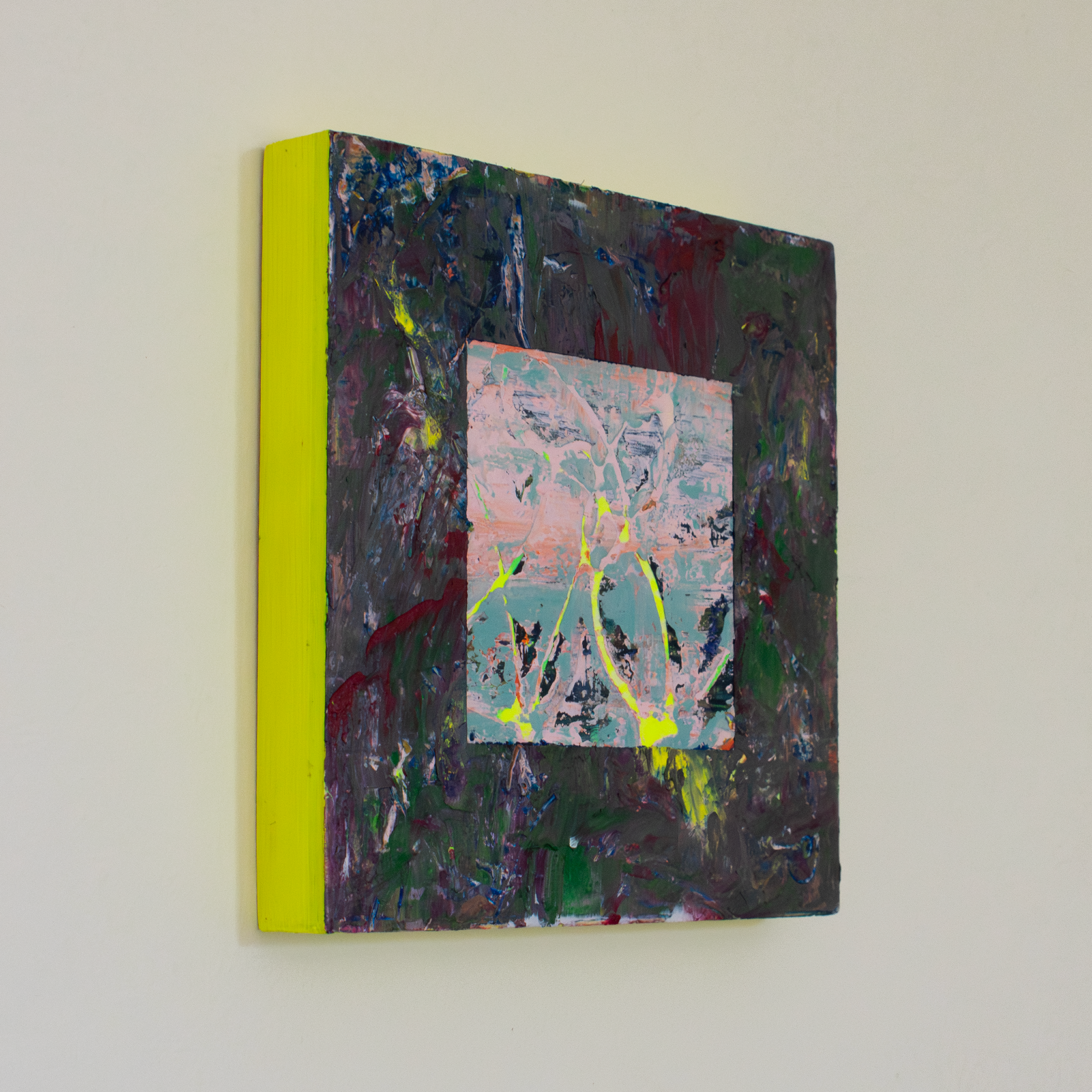 Right side view of textural abstract painting with thick impasto surface with colours of deep purple, blood red, green and yellow. In the centre there is a cut away square exposing a soft pink and blue textural underpainting with some thin areas of neon yellow peaking through. The edges of the painting are neon yellow and make a soft yellow glow against the while wall.