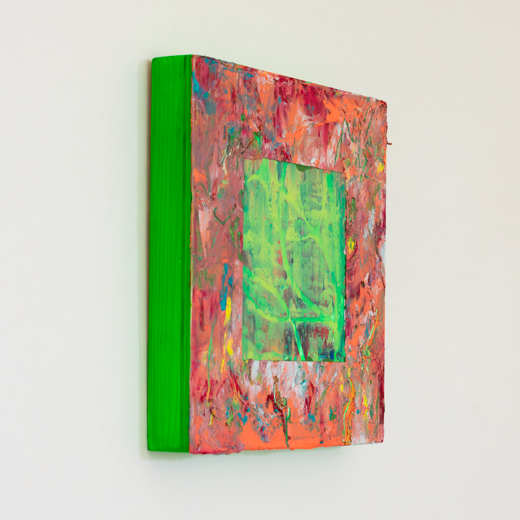 Left side view of textural abstract painting with thick impasto surface with colours of peach, orange, red and yellow. In the centre there is a cut away square exposing a green and yellow textural underpainting. The edges of the painting are neon green.