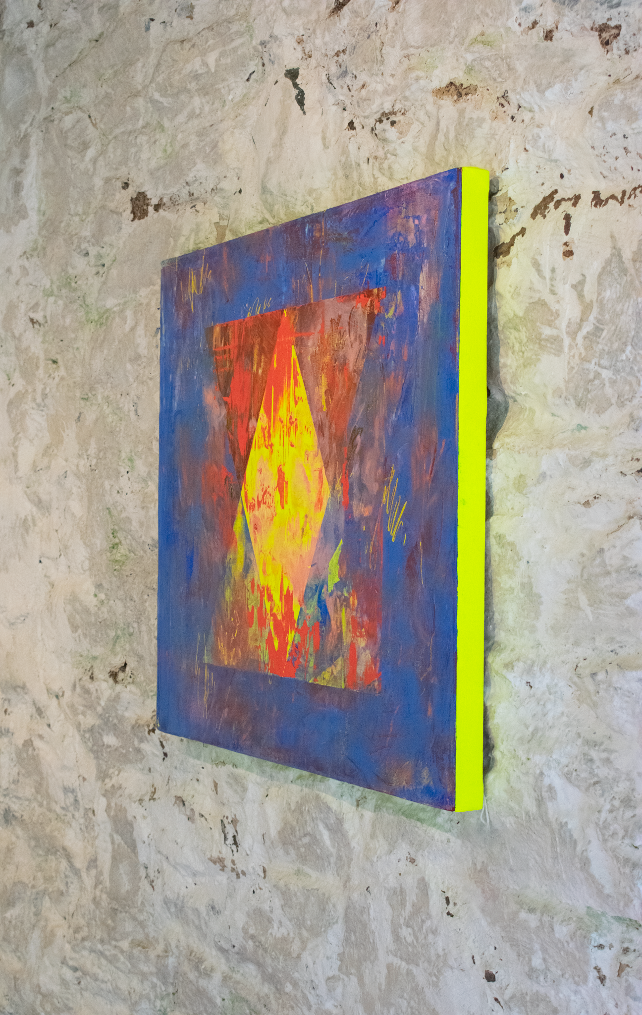 Side view of a textural oil painting with layered colours of blues, yellows, reds and brown. Gestural mark making on the surface of the painting with marks exposing a striking flourescent yellow layer of paint at the earliest layer. The edges are painted this same fluorescent yellow and glow against the clean white wall that the piece is hung on. Titled: .Untitled (A reason, a season, a lifetime) pt.2. Oil on canvas 60x60cm. £850