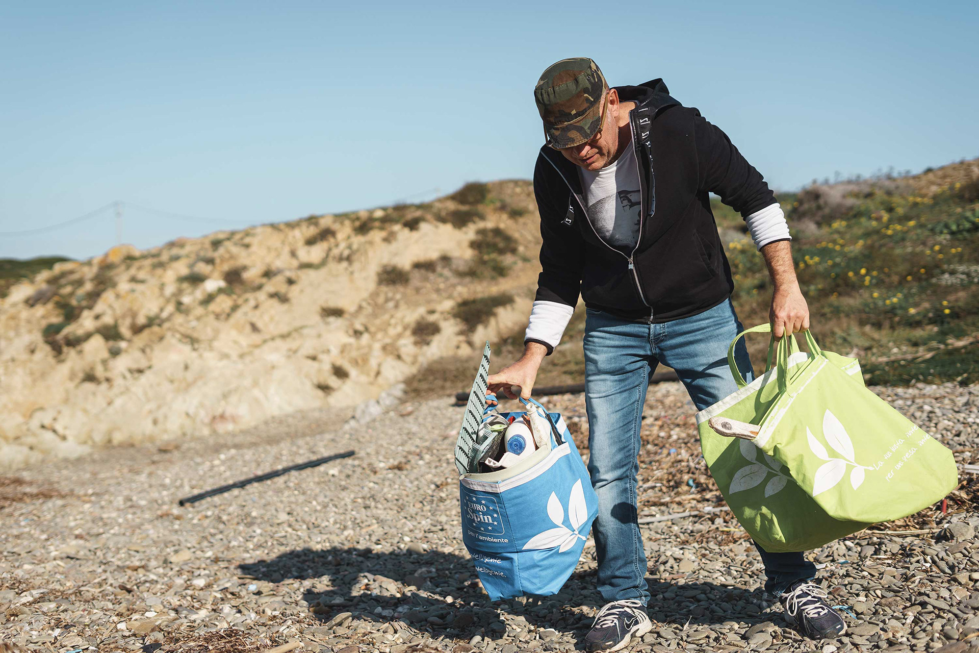 Environmental artist on rocky Sardinian coastline gathering materials for ocean pollution awareness sculpture