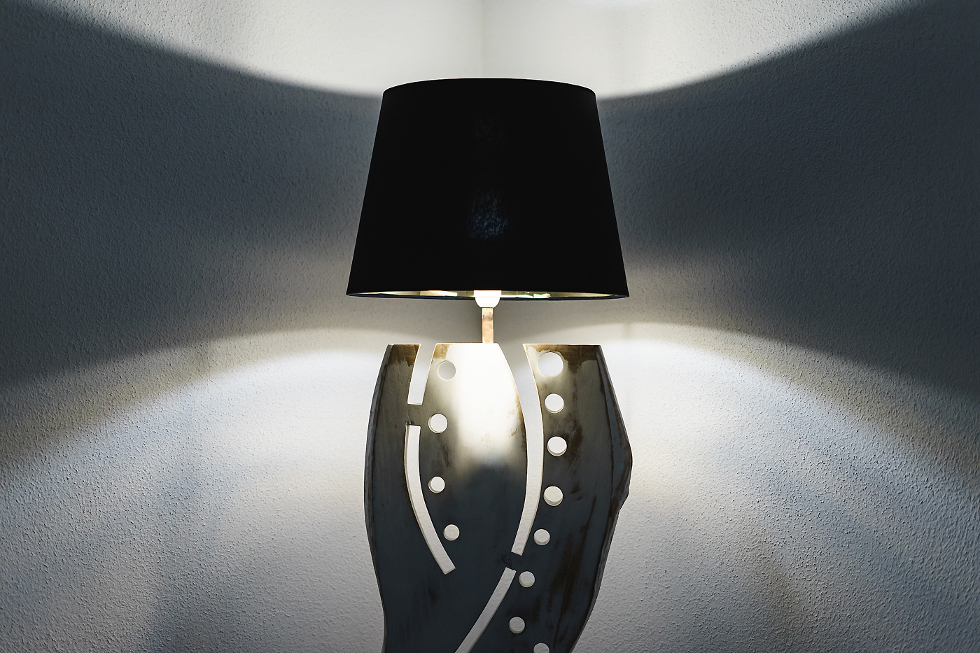 Illuminated vertical floor lamp by Scoobafish, casting symmetrical light across the wall through its carved openings.