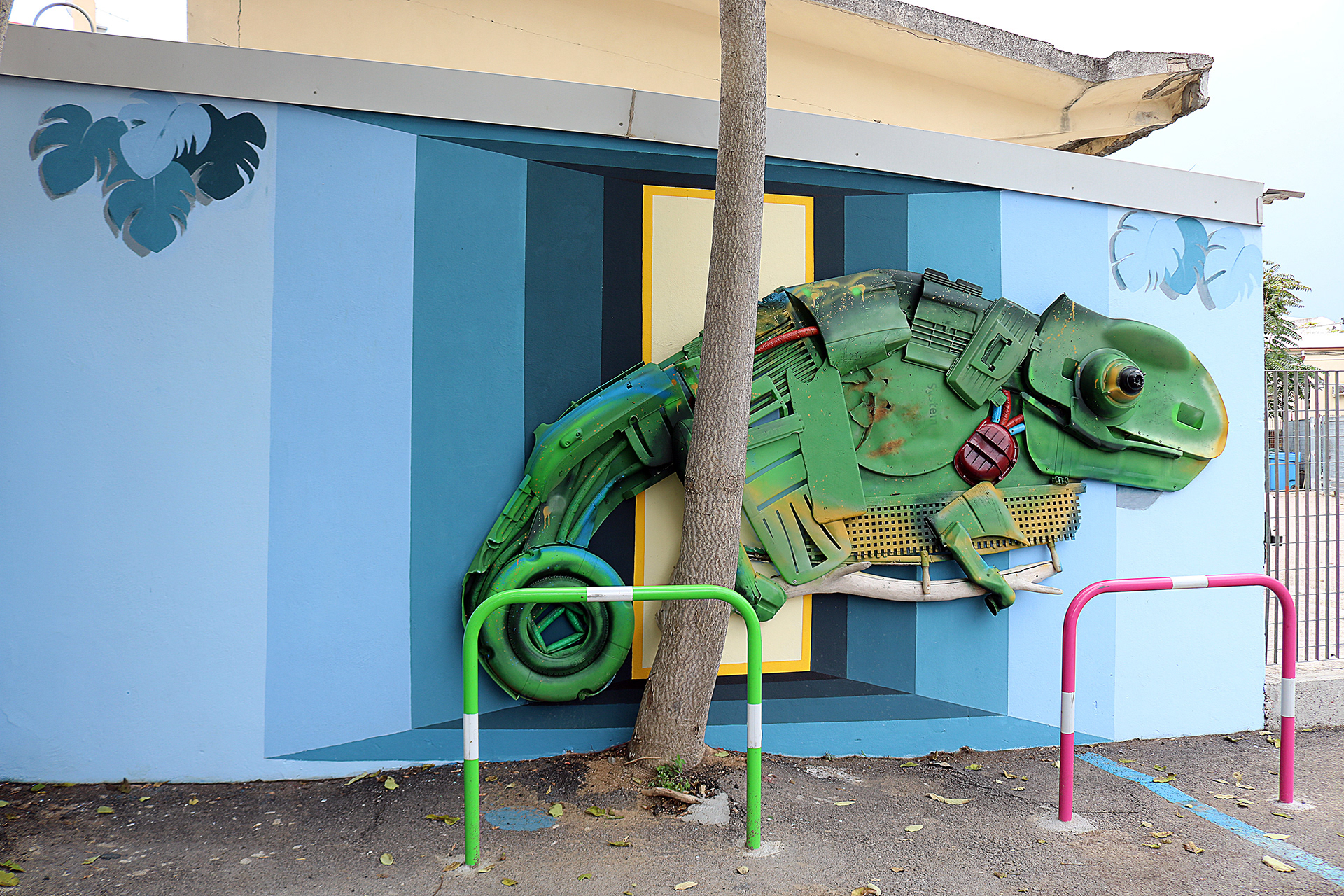 Wide view of Giant Chameleon integrated into the painted railway station wall and surrounding trees.