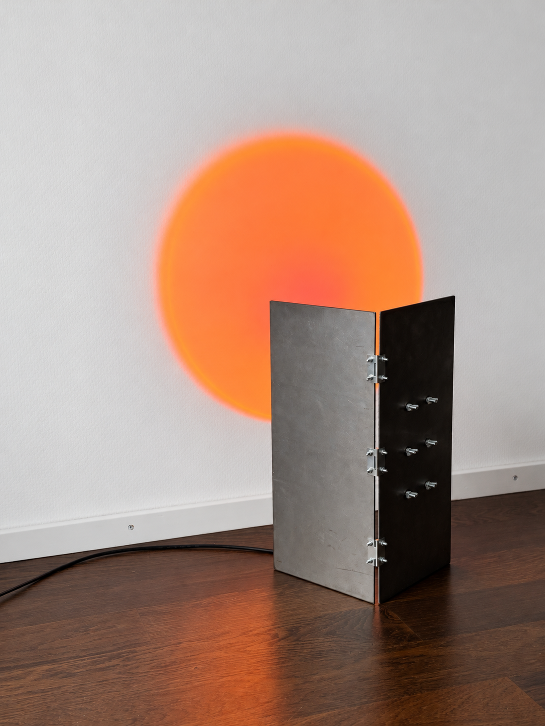 Claire Eppley, Atelier Eppley, Contemporary artist Zurich  Mixed media artist Switzerland  Contemporary sculpture Zurich  Abstract mixed media art  Sculptural wall art  Contemporary art Switzerland  Original contemporary artwork  Mixed media sculpture, Niseko Sunset Lamp, a contemporary light sculpture made of steel, projecting a glowing orange sunset onto your wall.