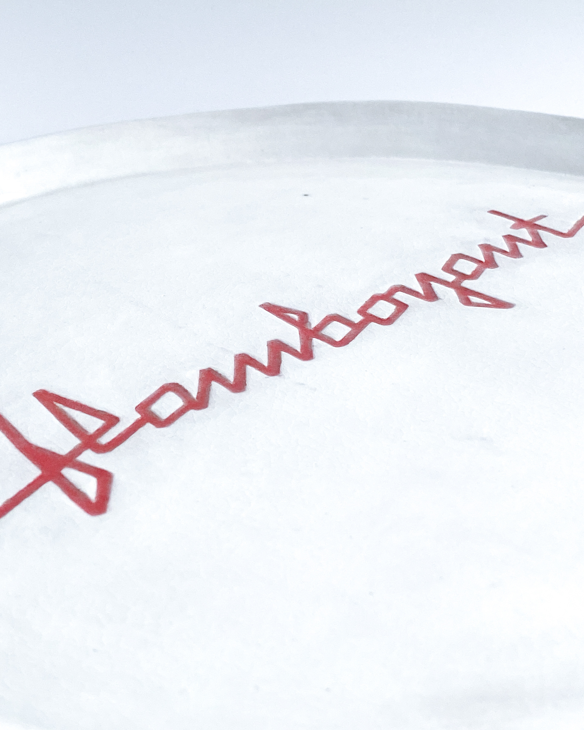 White glazed ceramic plate with angular red lettering spelling flamboyant across the centre
