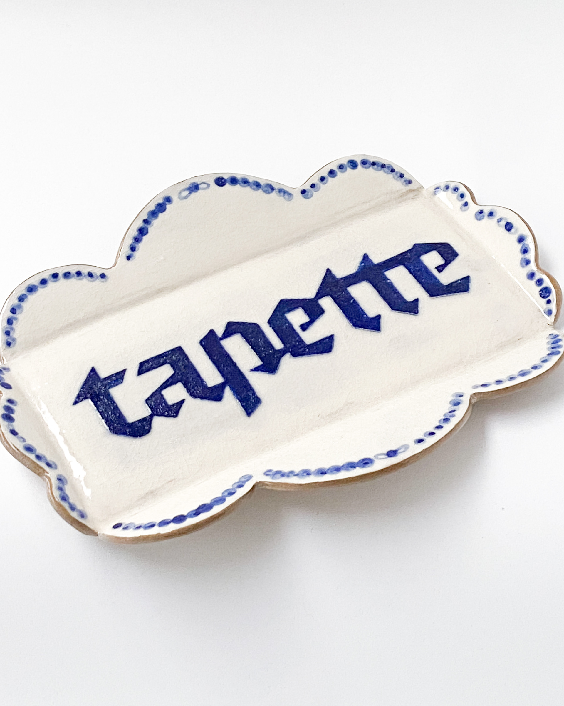 Small white and blue glazed ceramic tray with decorative scalloped sides, labelled tapette
