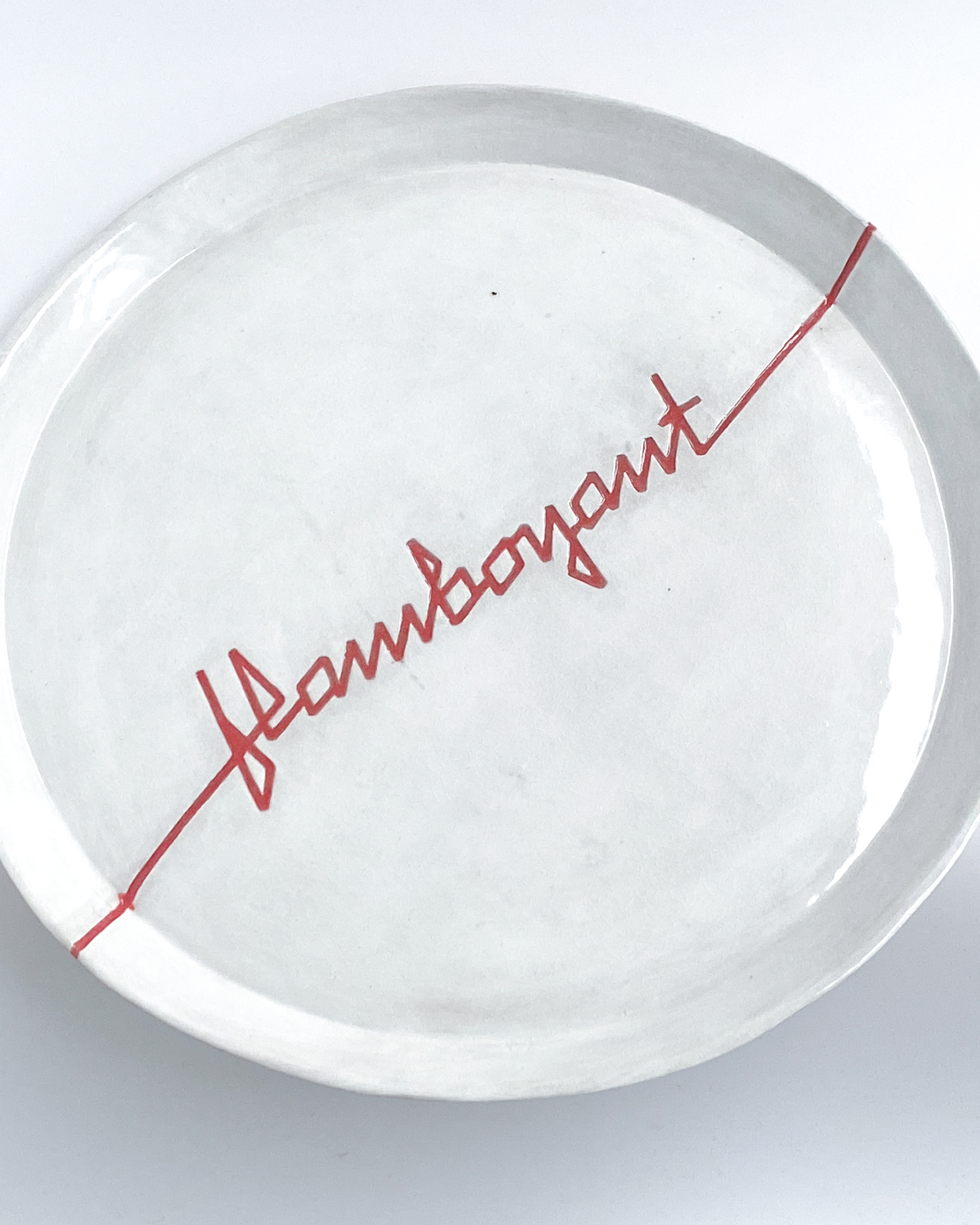 White glazed ceramic plate with angular red lettering spelling flamboyant across the centre