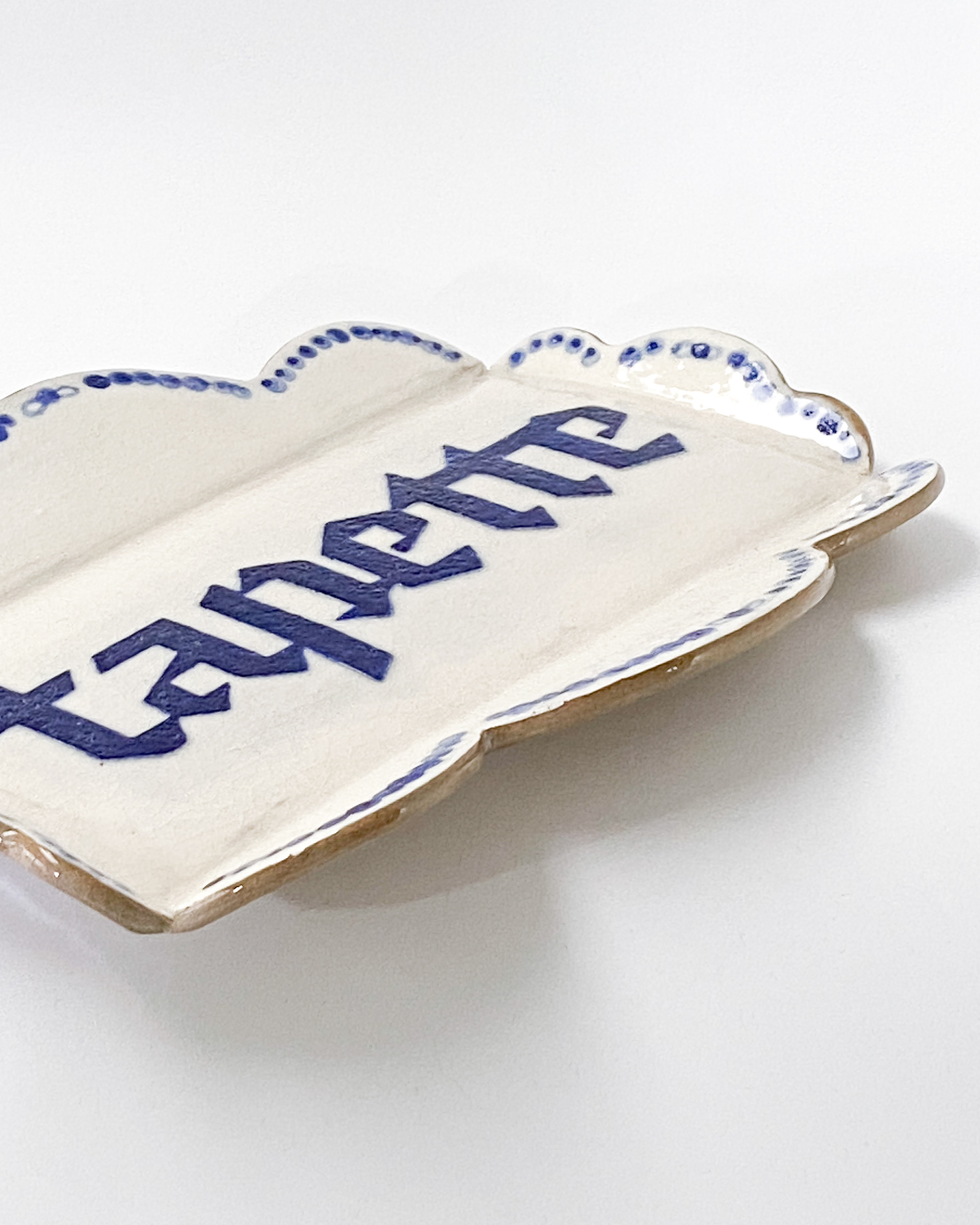 Small white and blue glazed ceramic tray with decorative scalloped sides, labelled tapette