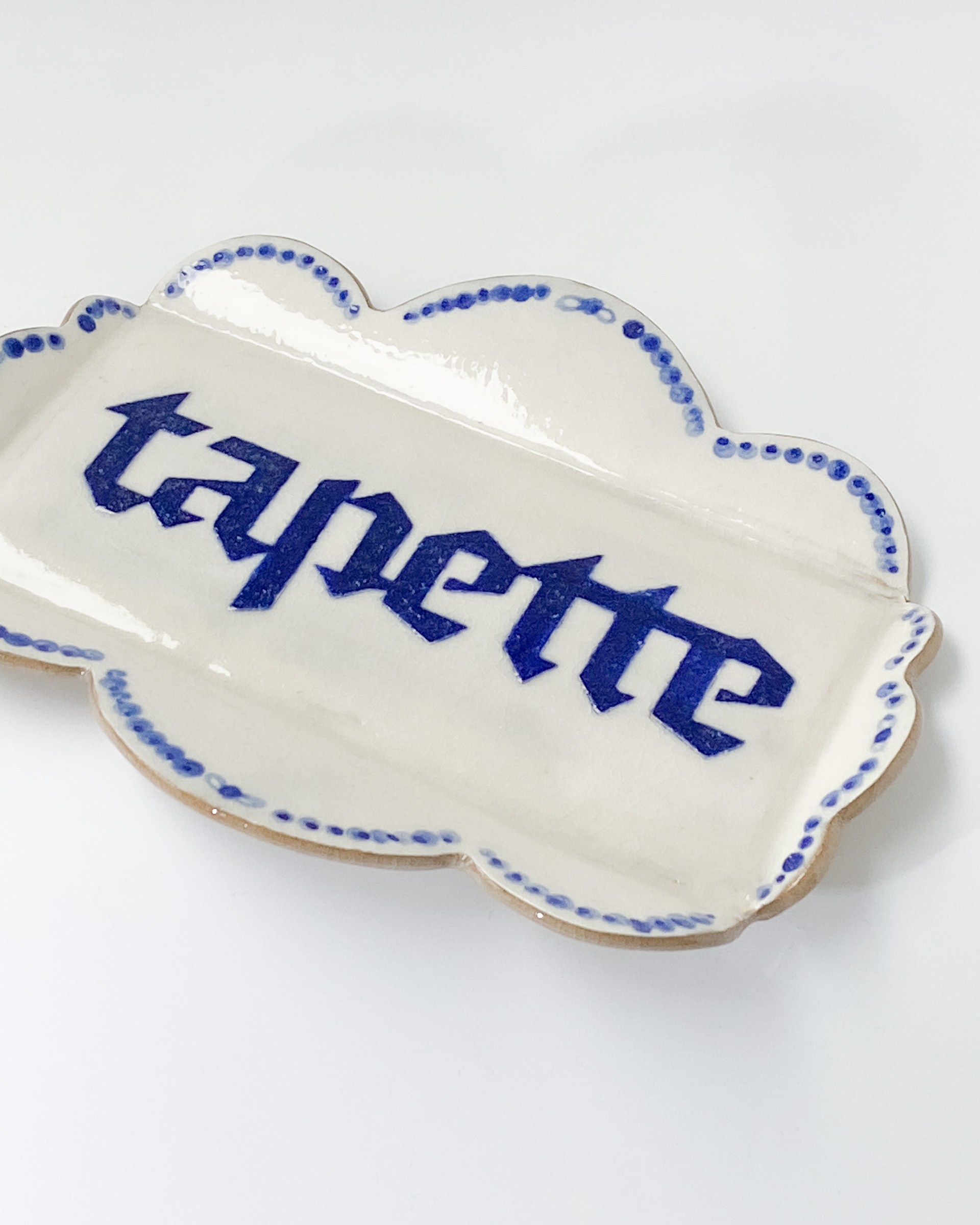 Small white and blue glazed ceramic tray with decorative scalloped sides, labelled tapette