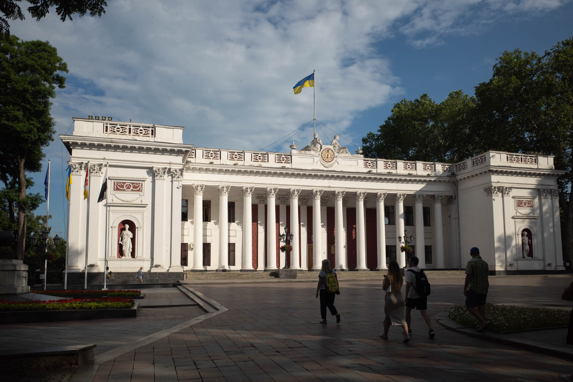 The Ukrainian national flag flies over the Odesa City Hall building as people walk across the square in front of it in Odesa, Ukraine, on June 12, 2026. The neoclassical building on Dumska Square houses the city council of Odesa