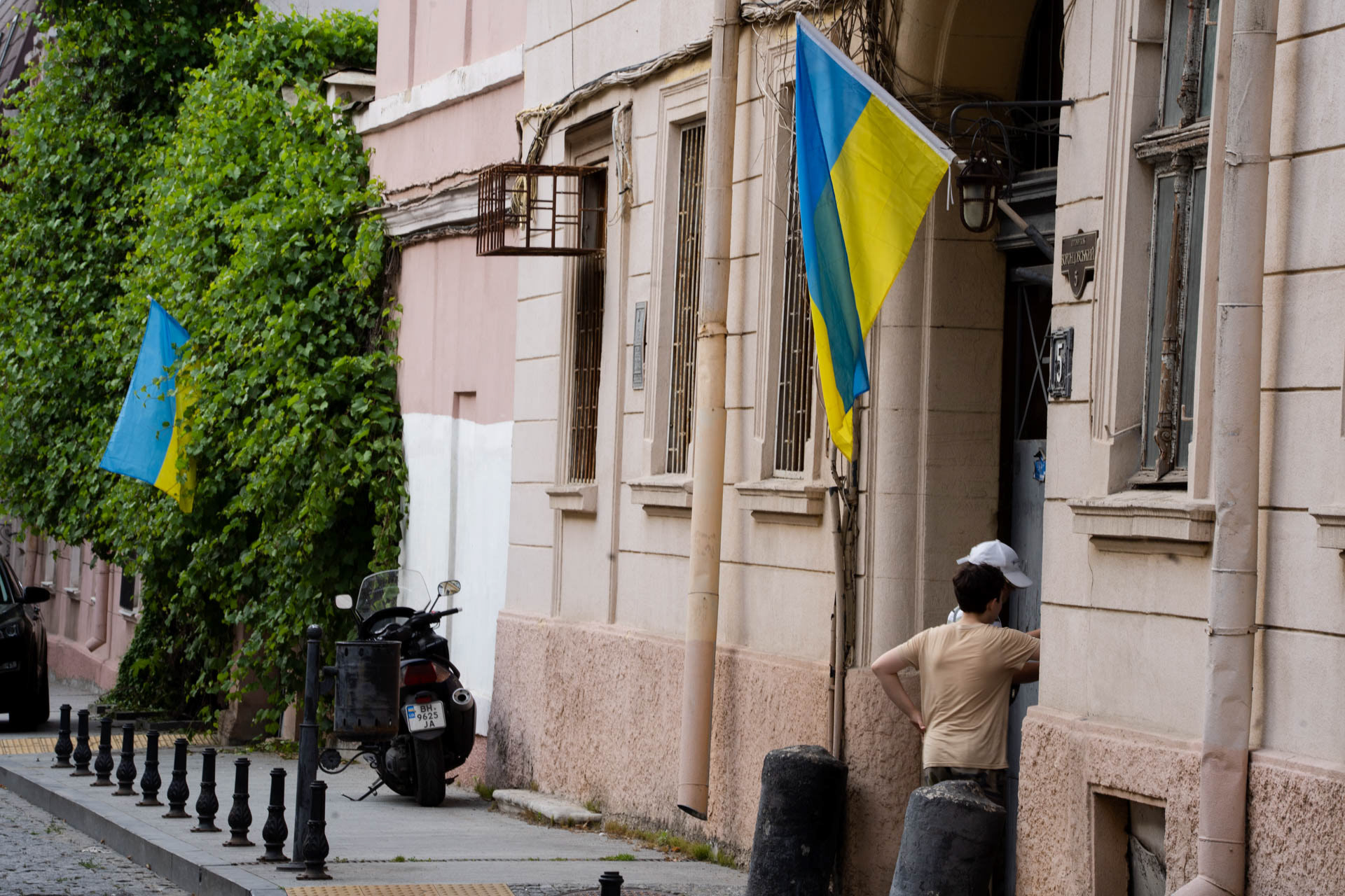 Two boys enter a residential building beneath Ukrainian national flags hanging from the facades along a street in central Odesa, Ukraine, on June 12, 2026. The blue and yellow flag has become a widespread symbol of national identity displayed across Ukrainian cities during the Russian invasion of Ukraine.