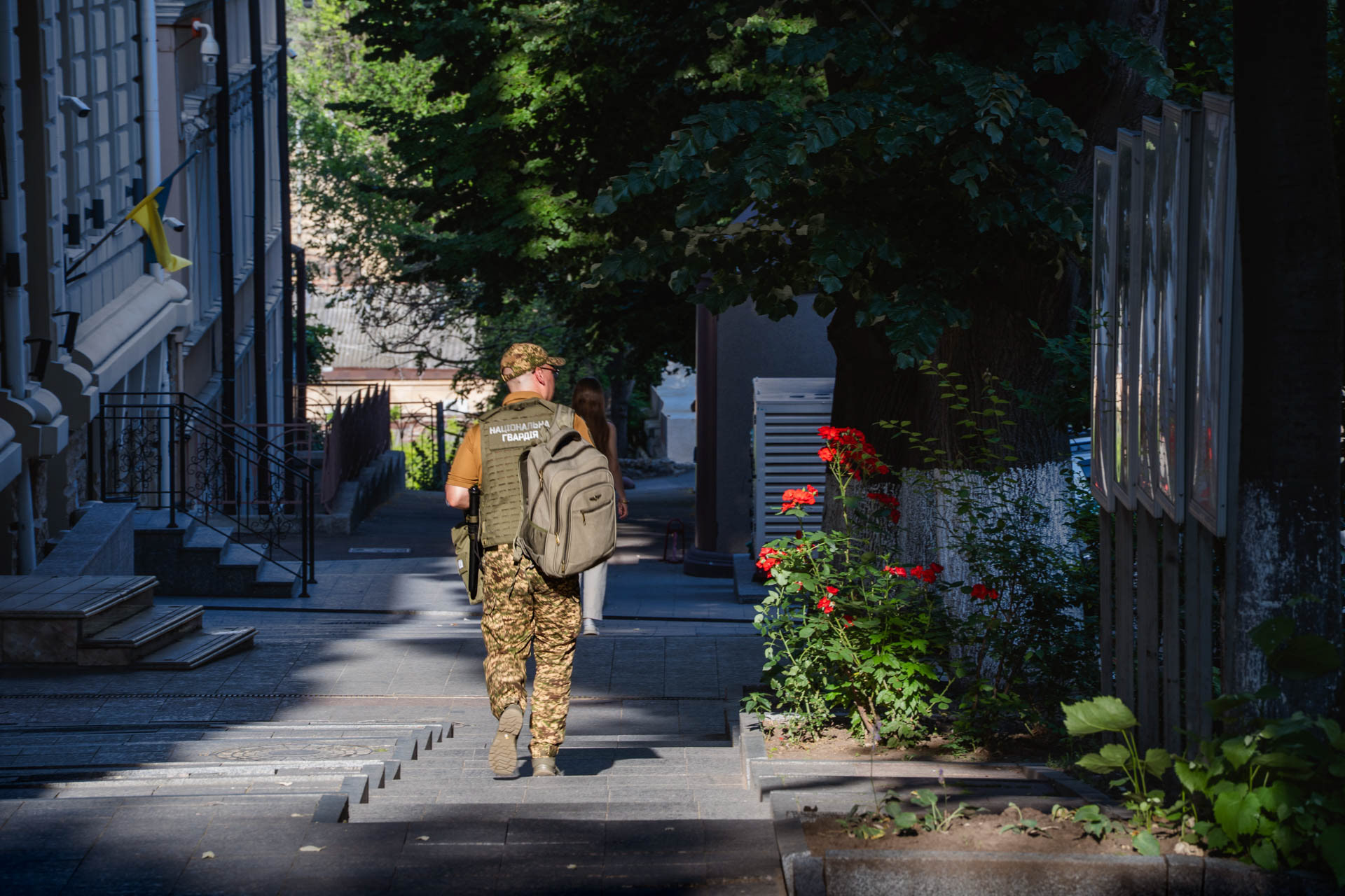 A Ukrainian soldier carries a backpack as he walks up a staircase in central Odesa, Ukraine, on June 12, 2026, as another pedestrian passes ahead of him. The patch on his vest reads "Національна Гвардія" (National Guard of Ukraine).