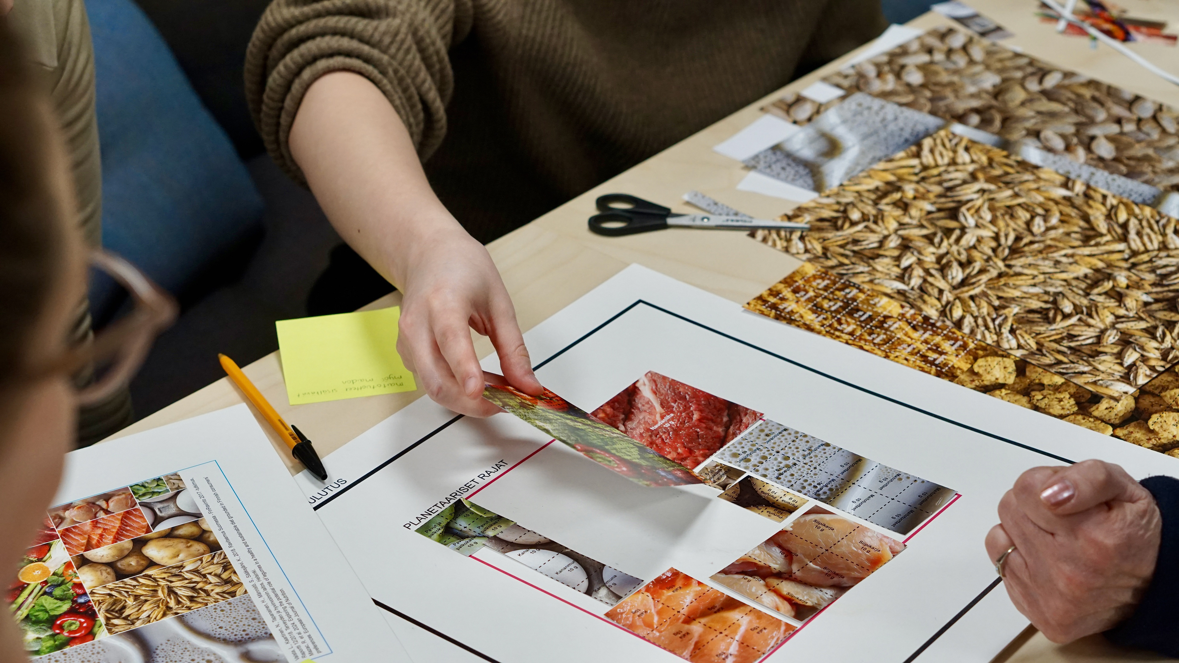 Close-up of participants' hands placing food item pieces onto the Planetary Plate game board. The cut-out pieces vary in size to represent the climate impact of different foods