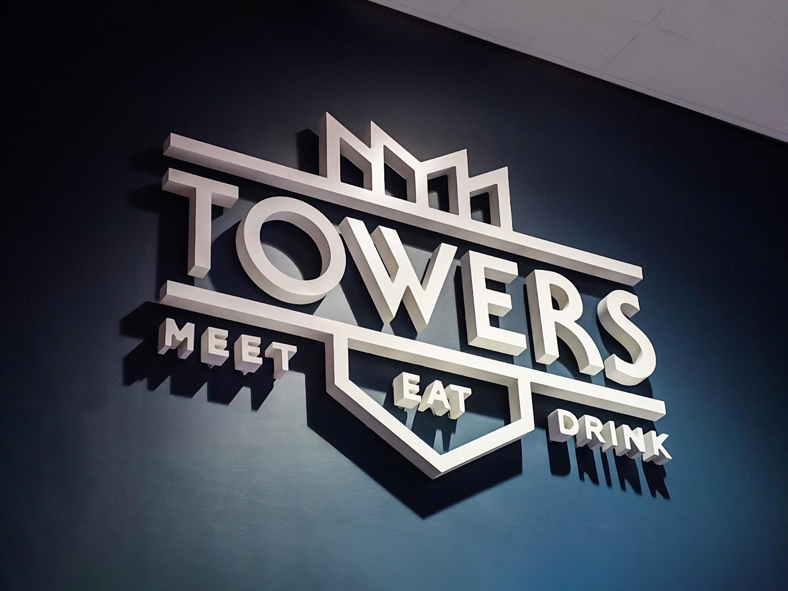 A 3 dimensional logo for Towers including the words "meet, eat, drink" mounted on a wall.