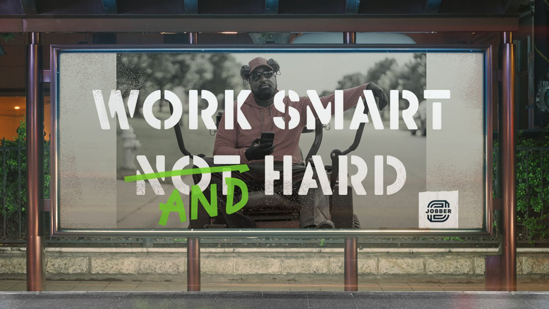 A billboard that reads "work smart not hard" but "not" is crossed out and "and" is written over top. A man on a riding lawnmower is in the background, Jobber logo in the bottom corner.
