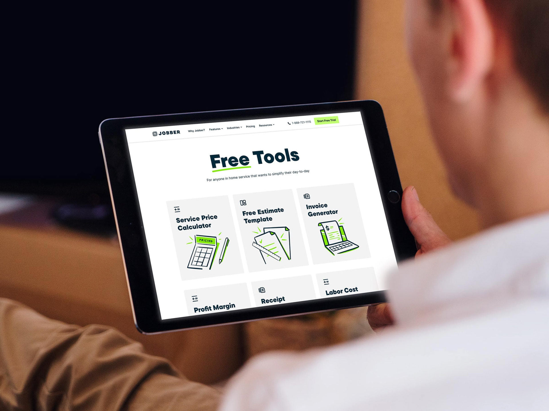 A person holds an iPad. On screen is a Jobber webpage that reads "Free Tools" featuring illustrations.