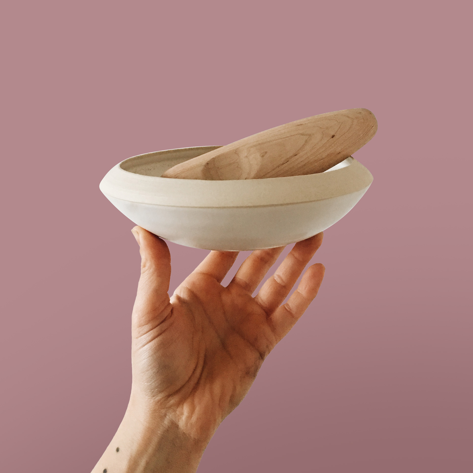 A hand holds up a ceramic mortar with a wooden pestle inside.