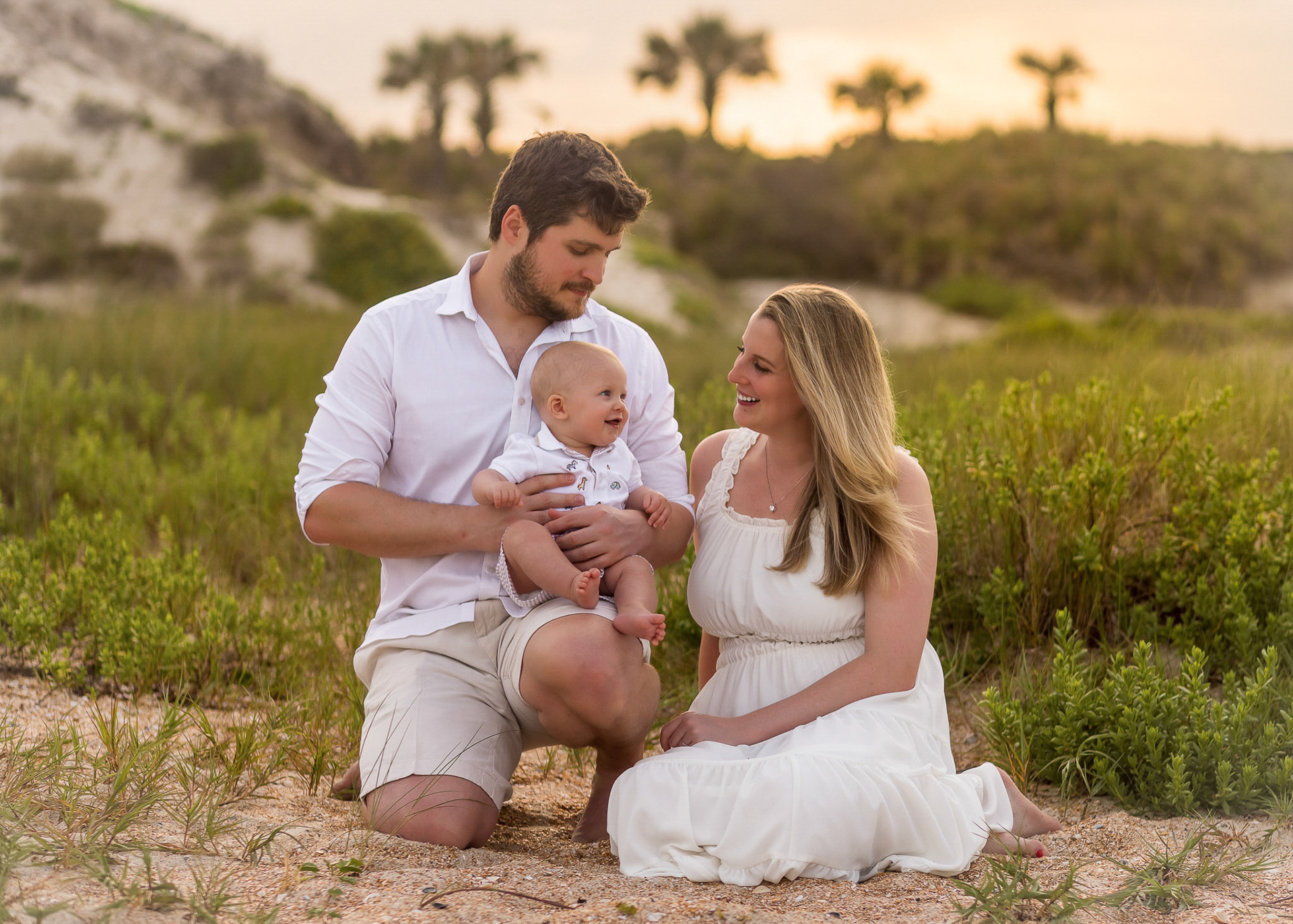 Mom & Dad laughing with their adorable baby at the dunes during Sunset Beach Family Photo Session at  Ponte Vedra Beach
