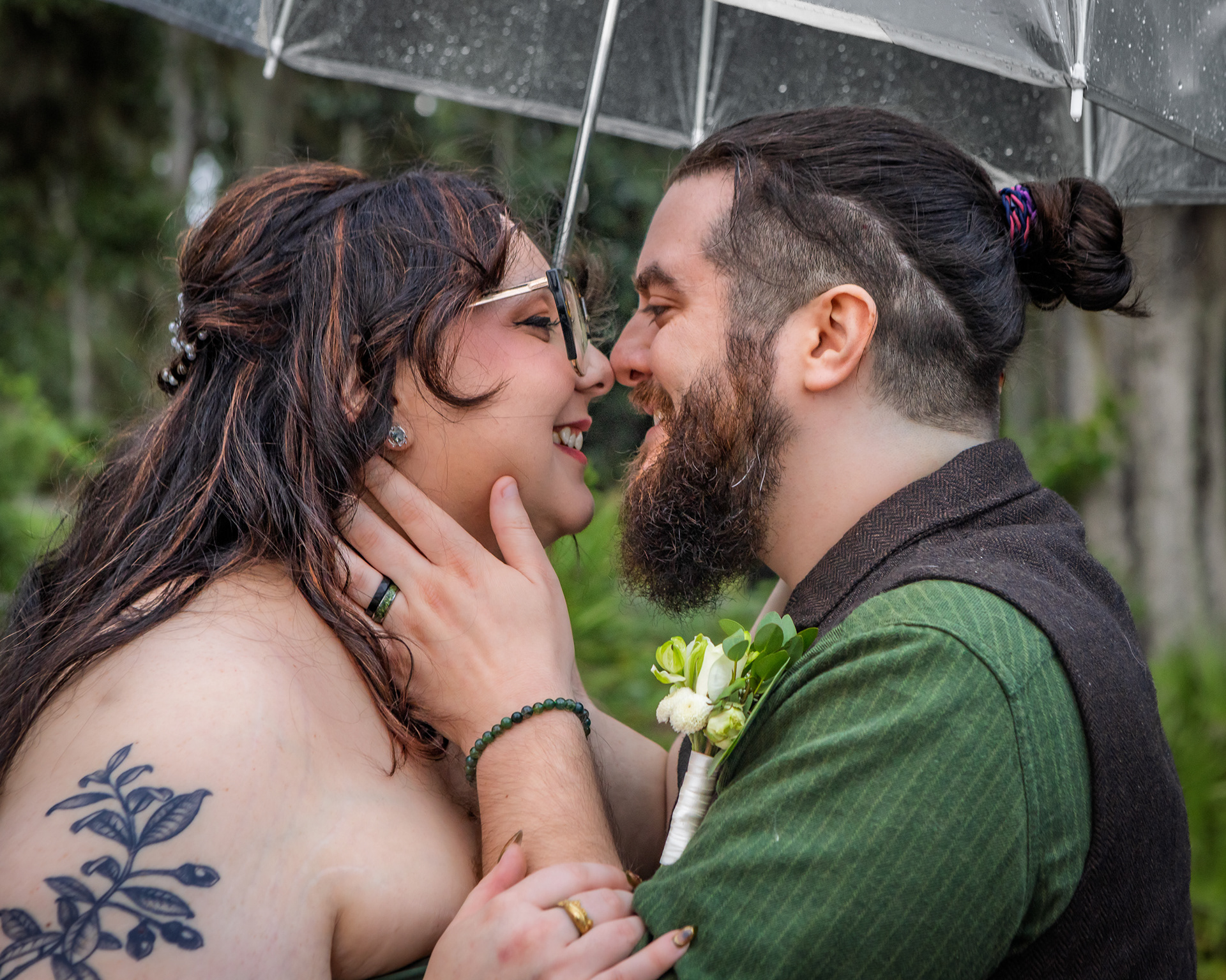 Joyful bride and groom kissing under a clear umbrella during rainy day wedding portraits session at Riverwalk Park St. John's River
