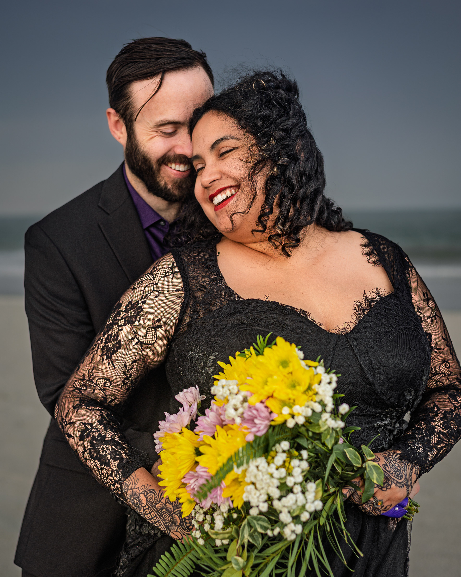 Joyful couple in black wedding lace gown and suit on Villano Beach during stormy skies