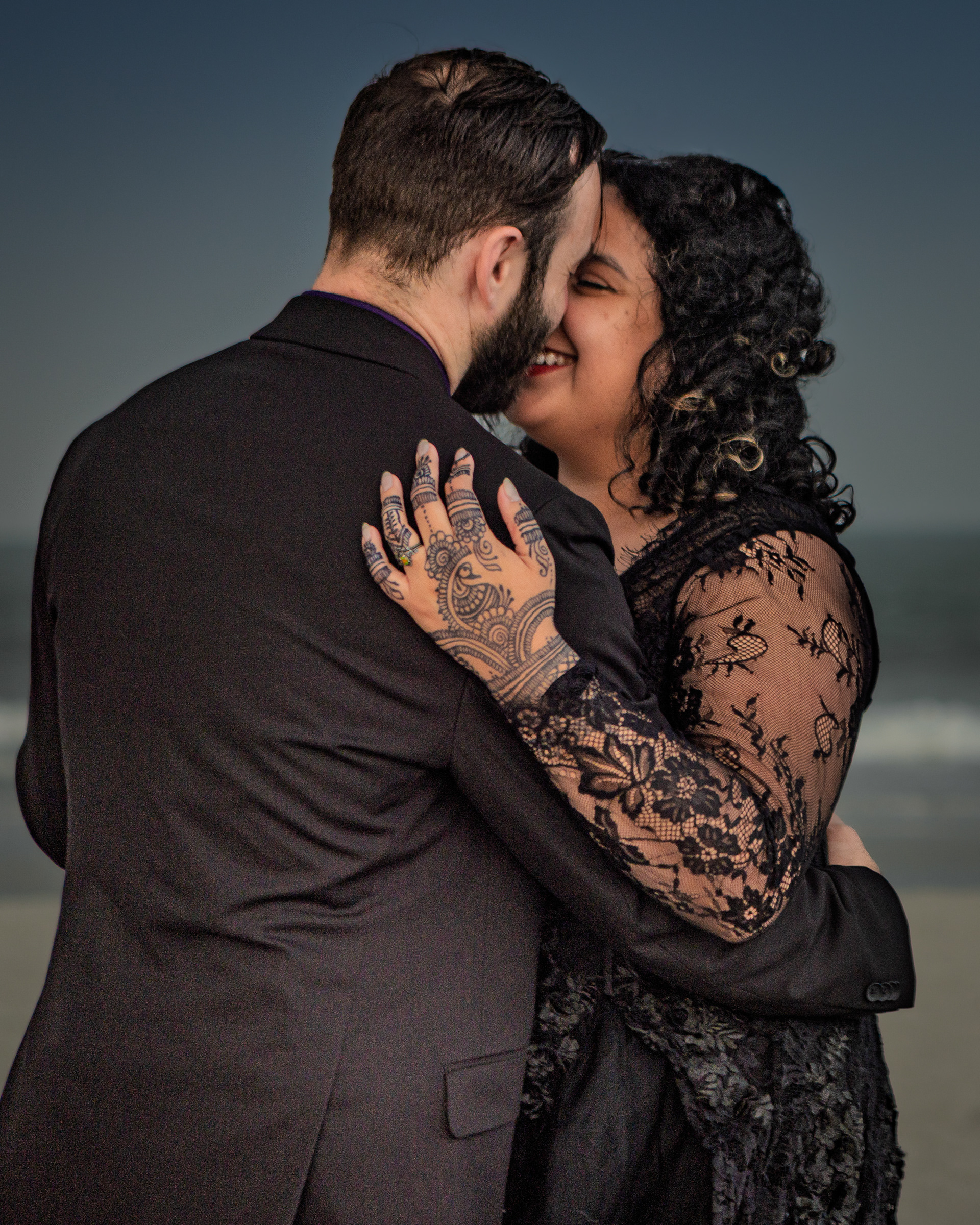 Newlyweds  in black wedding gown and suit embracing on Villano Beach during stormy skies