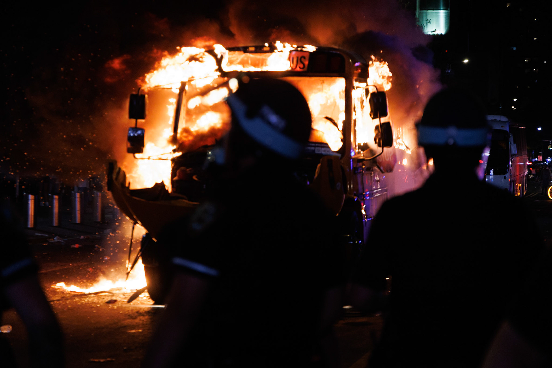 Silhouetted Figures Watch Burning Bus at Night