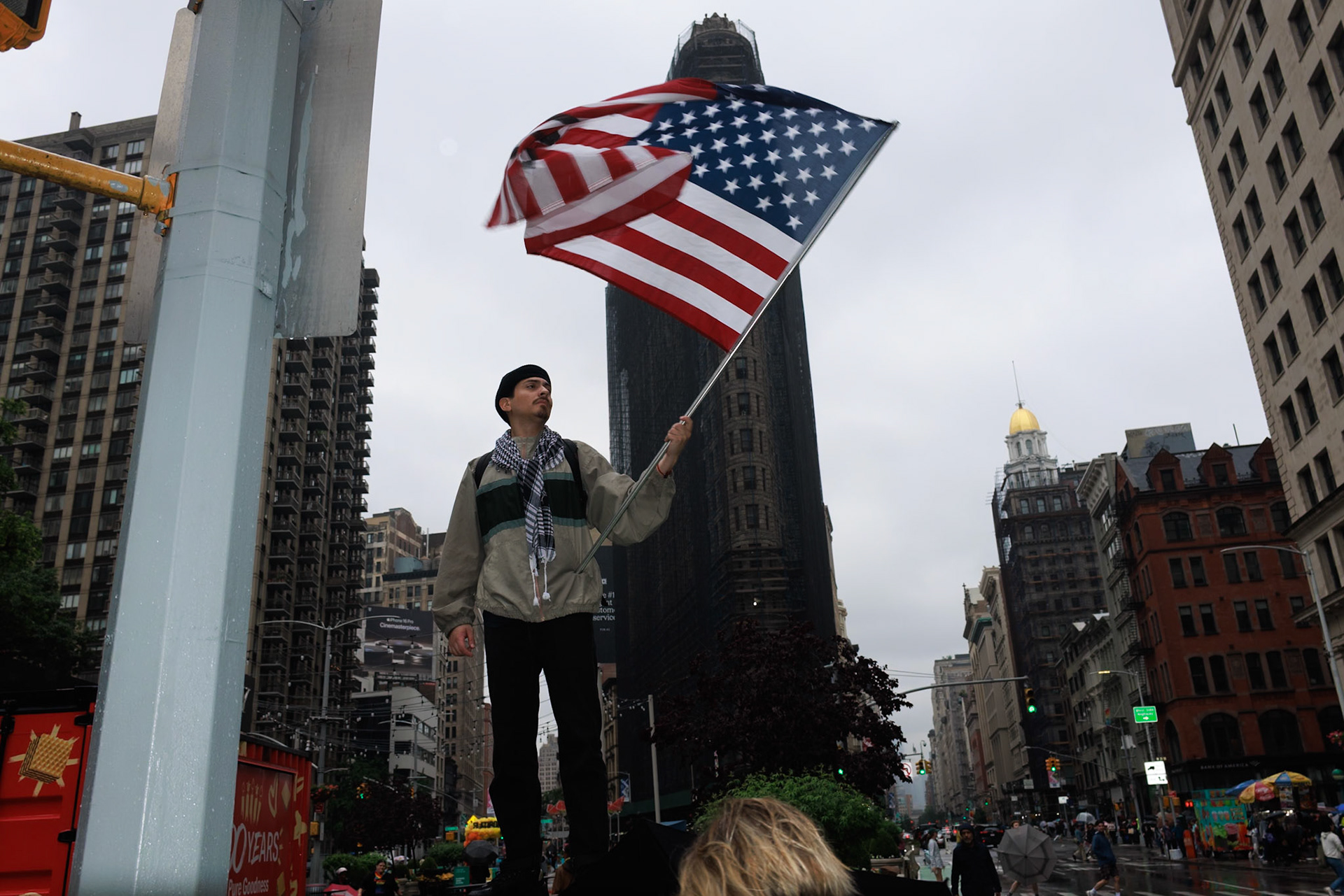 Man Holds American Flag Above Crowd in Rainy City Street