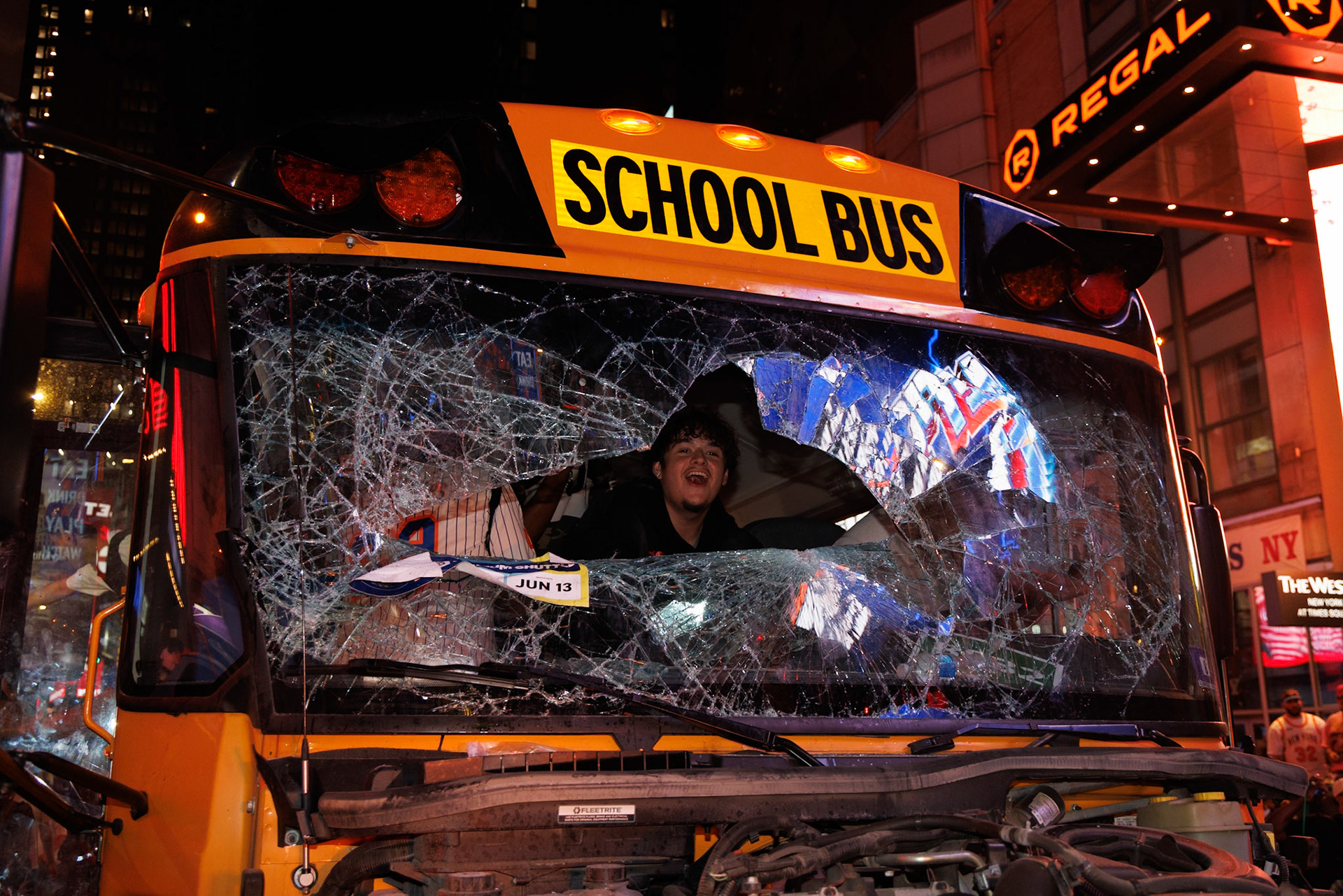 Smiling Person Pokes Head Through Shattered School Bus Windshield